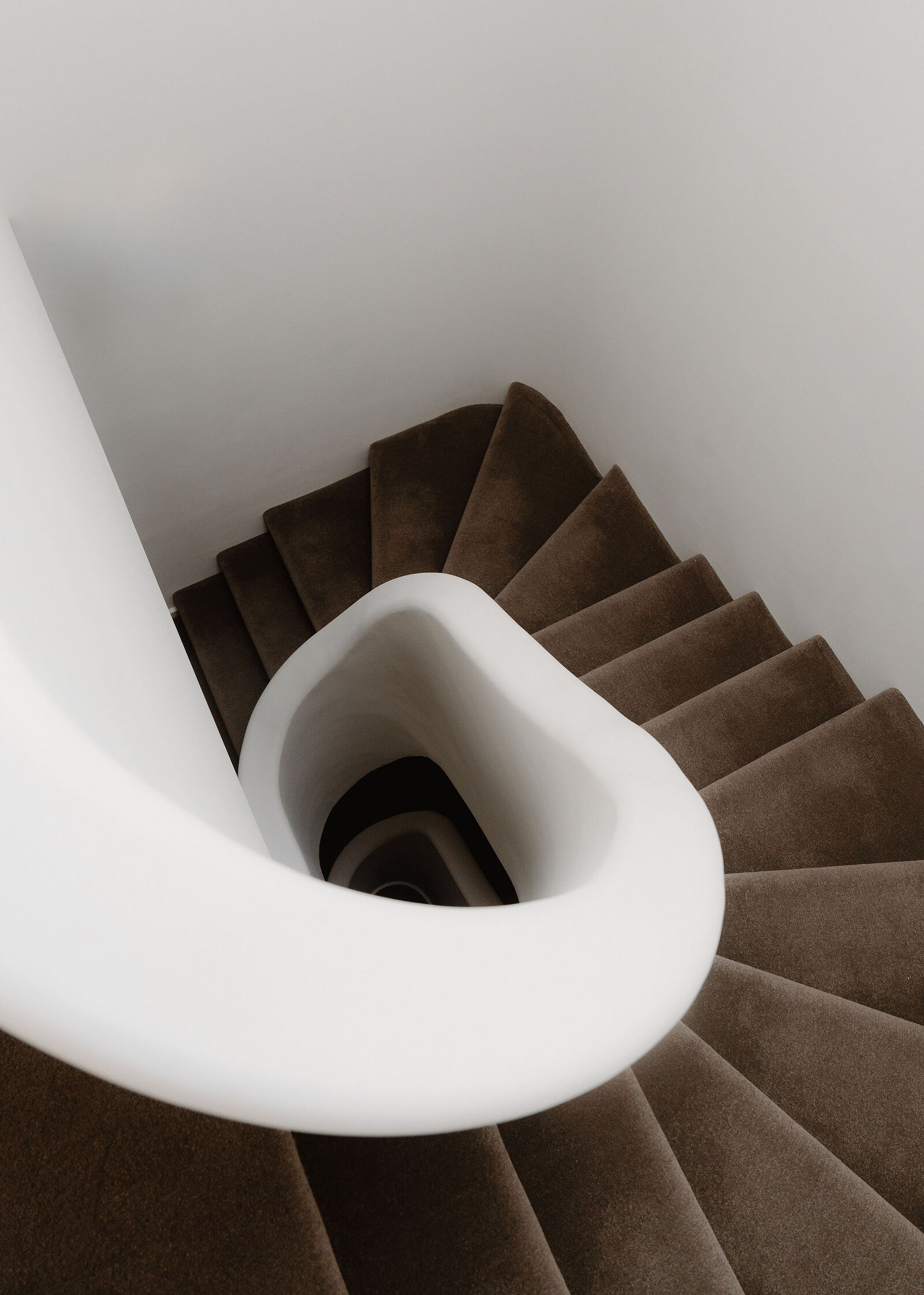 Looking down the stairwell: the white plaster rail spirals round carpeted steps.