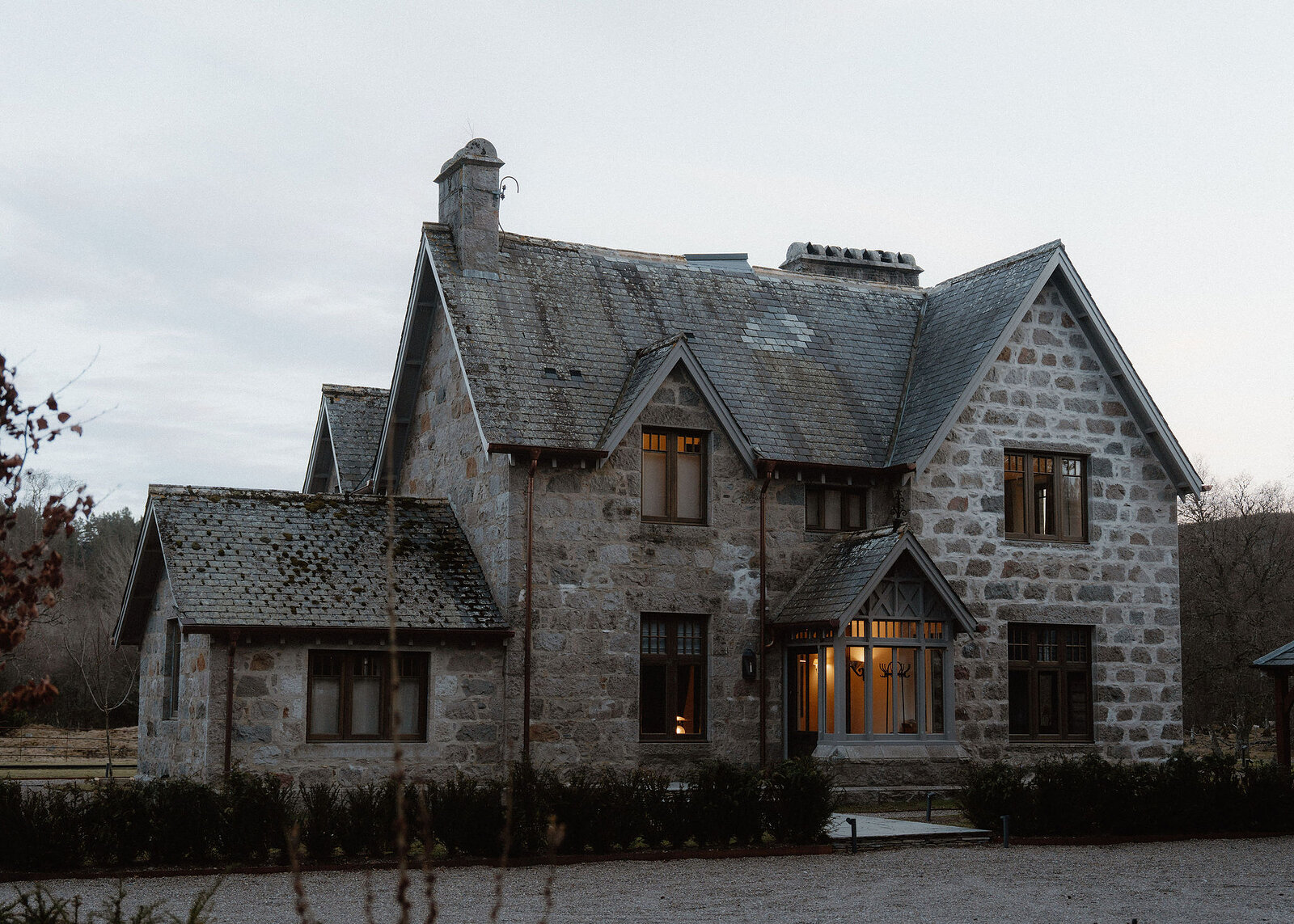 A landscape view of Faunoran House at dusk: granite walls, steep slate gables and tall chimneys, the porch lit.