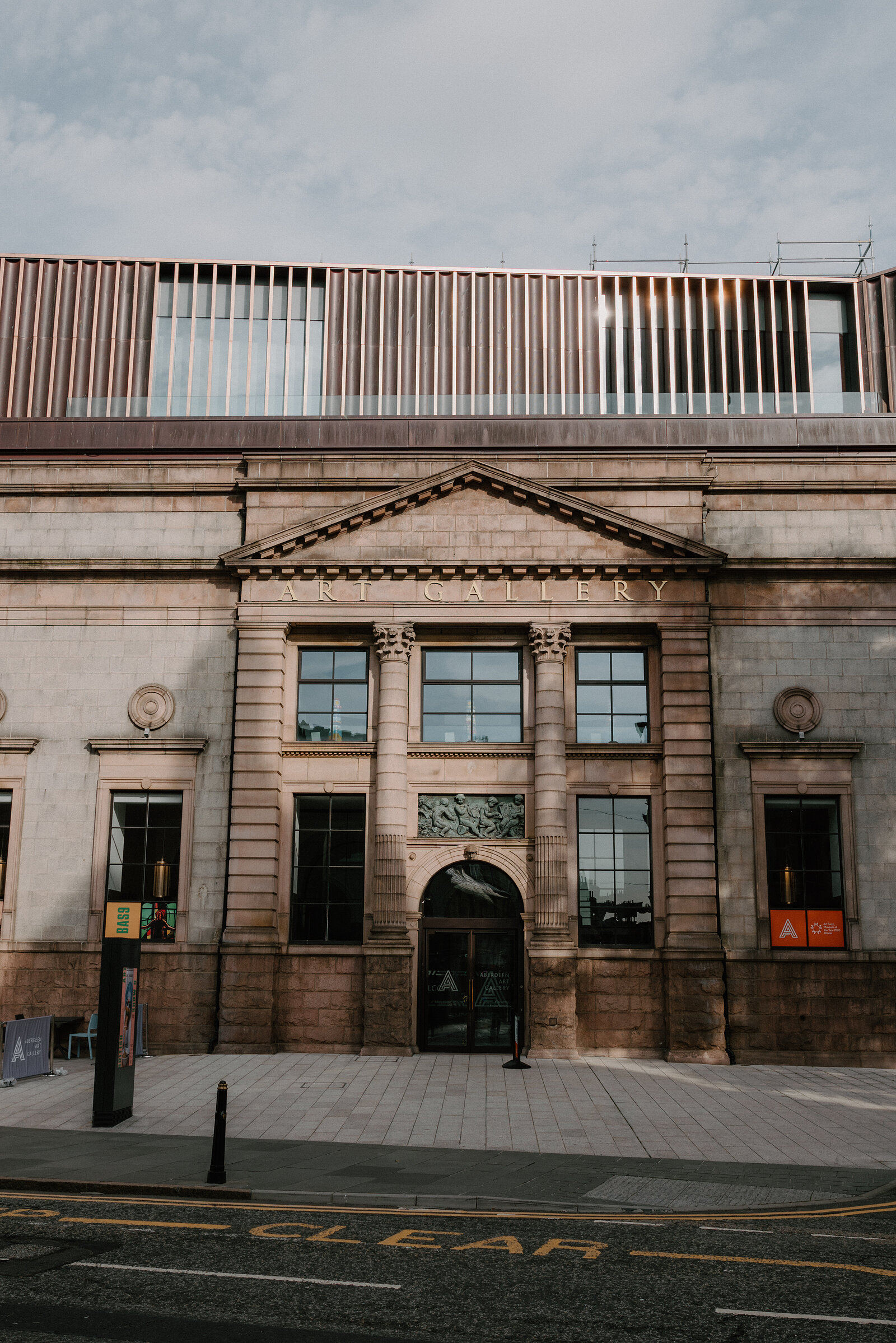 A sandstone Art Gallery building with pillared entrance and pediment, banners hanging beside the doorway