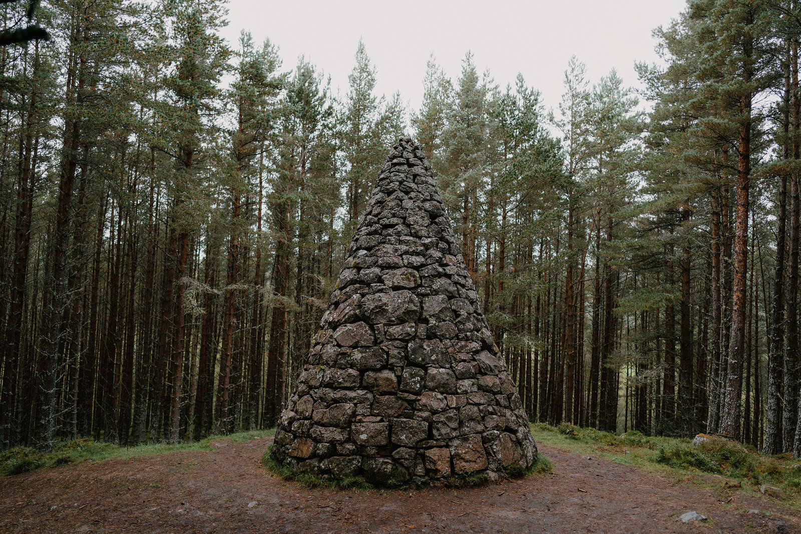A stone cairn shaped like a cone standing in a pine forest clearing