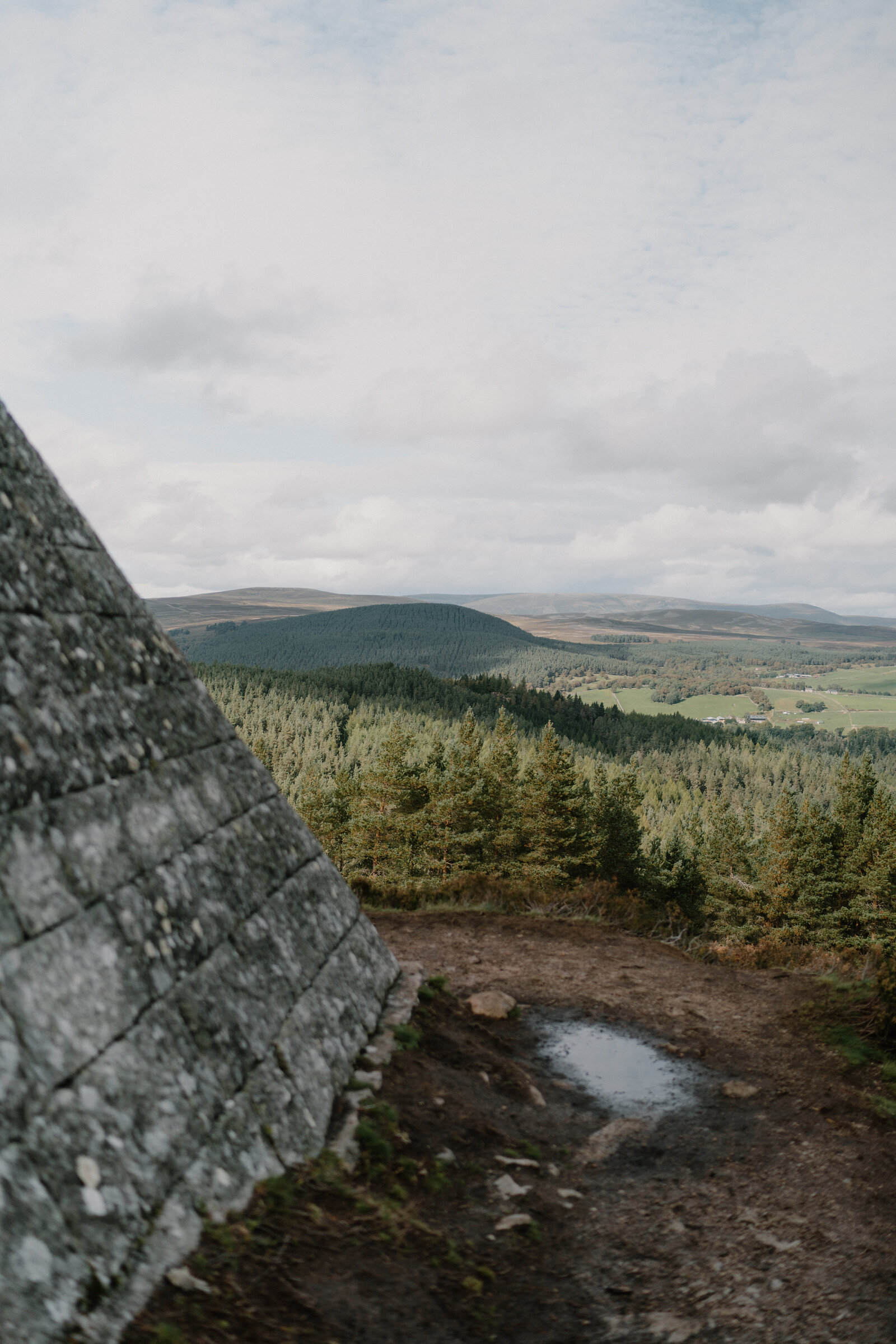 The lichened granite corner of Prince Albert's pyramid, and beyond it the view over the pines to fields and hills.