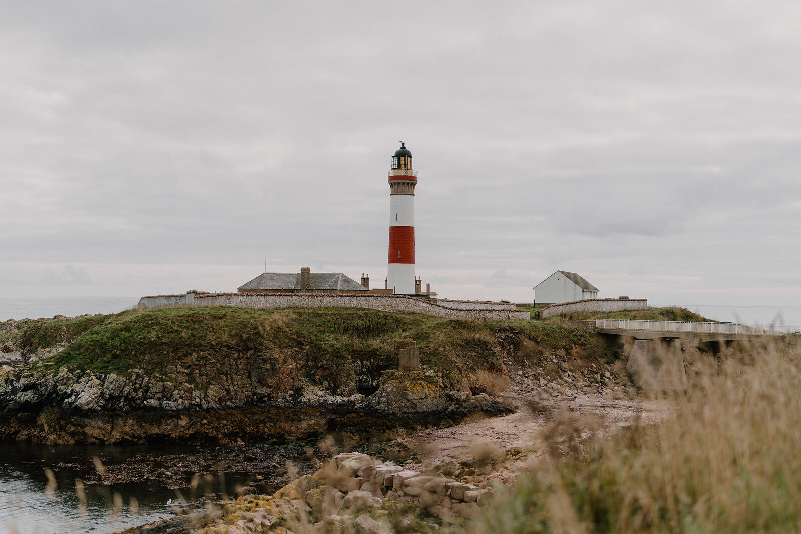 A red and white striped lighthouse standing on a rocky headland above the sea