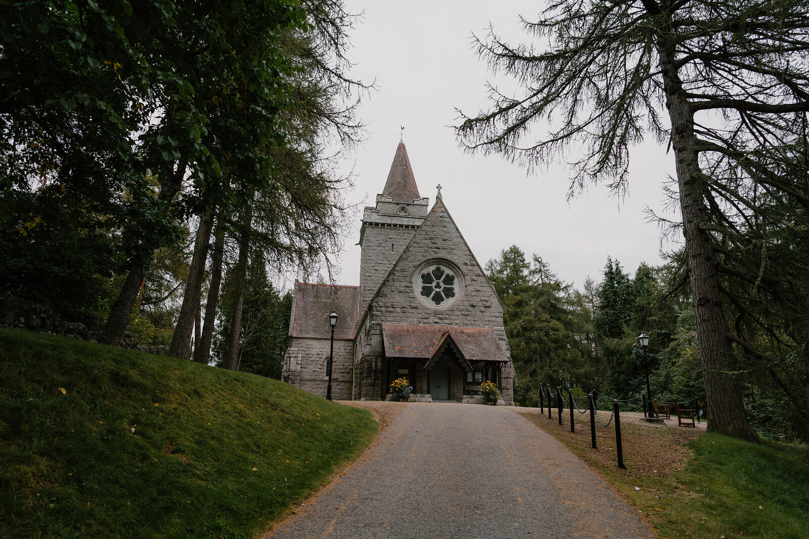 A stone church with a spire standing at the end of a tree-lined drive