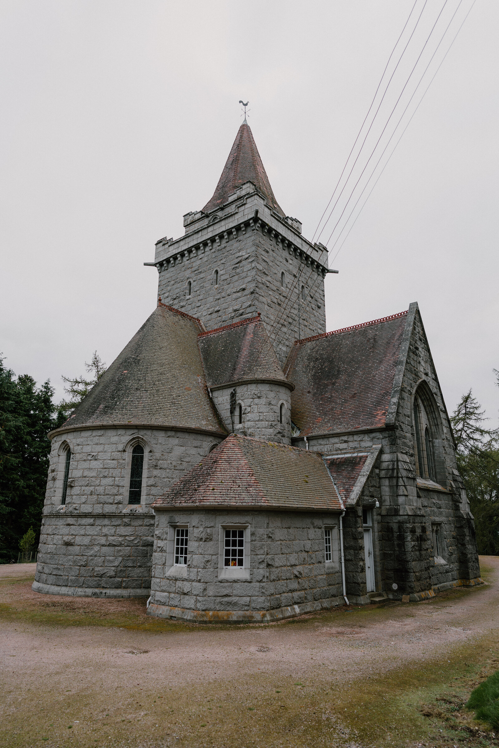 A stone church with a castellated tower and pointed spire, gravel paths leading around it