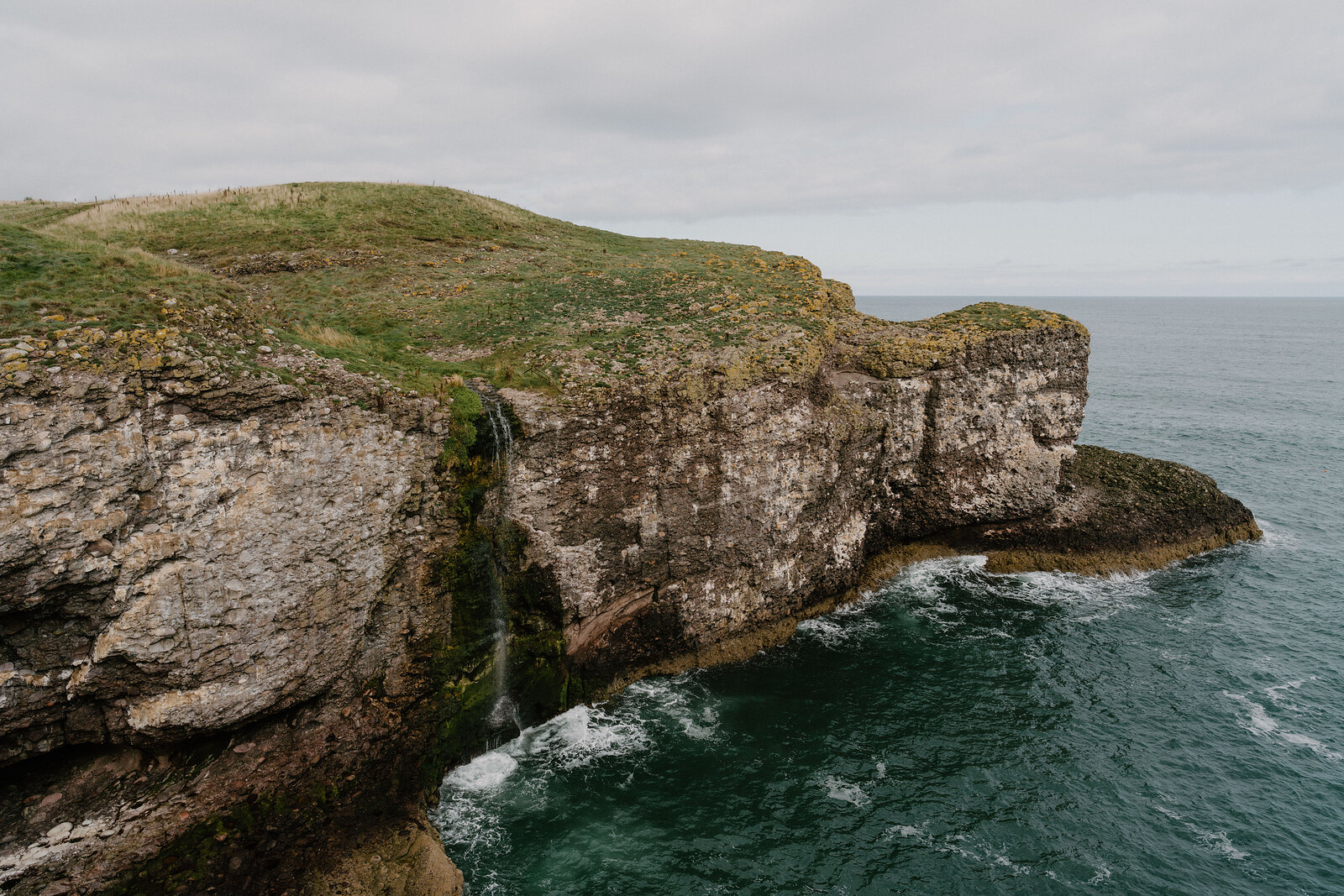 A grassy headland with a small waterfall spilling into the sea, cliffs rising on either side