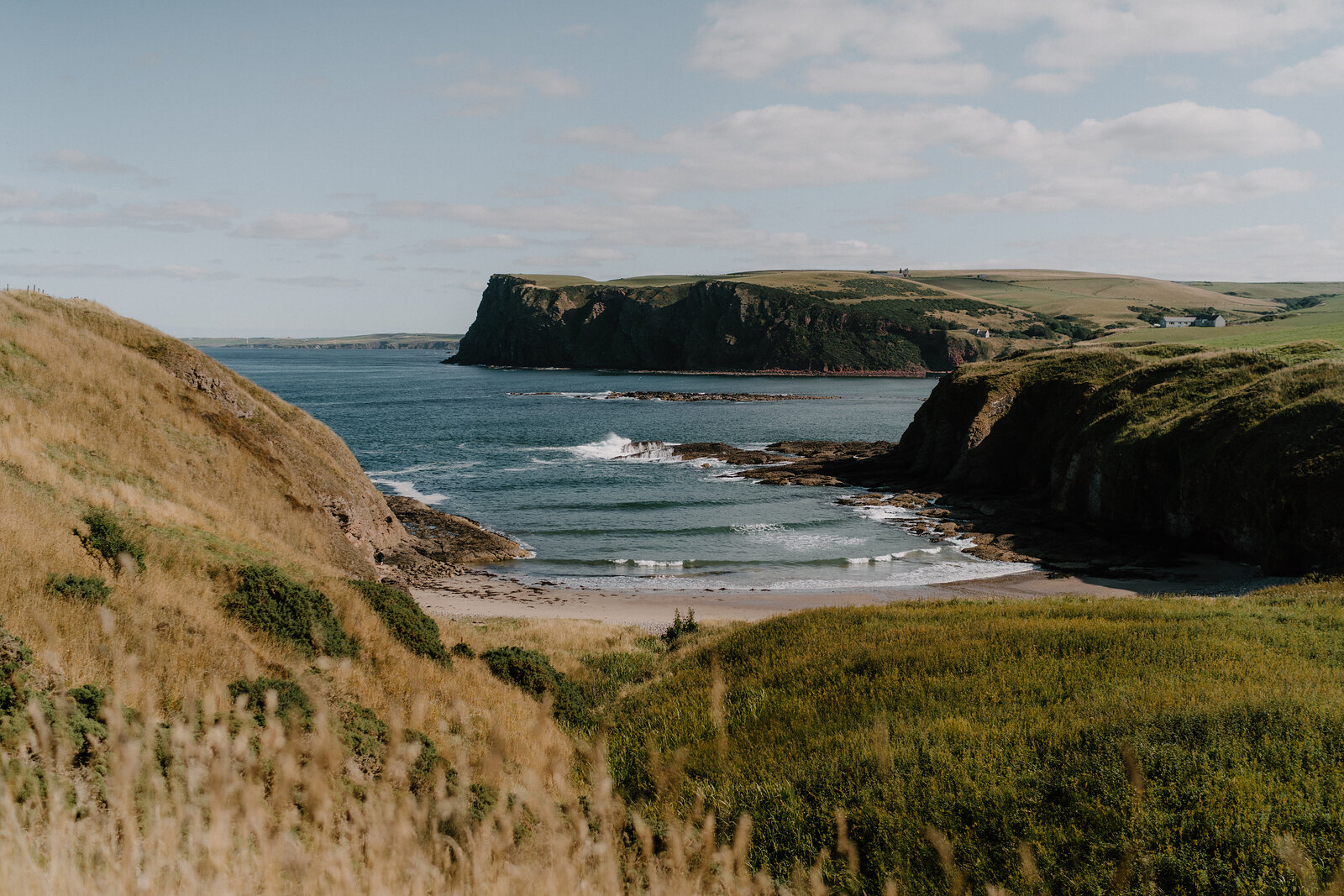 A sandy beach tucked between grassy headlands, waves breaking gently on the shore
