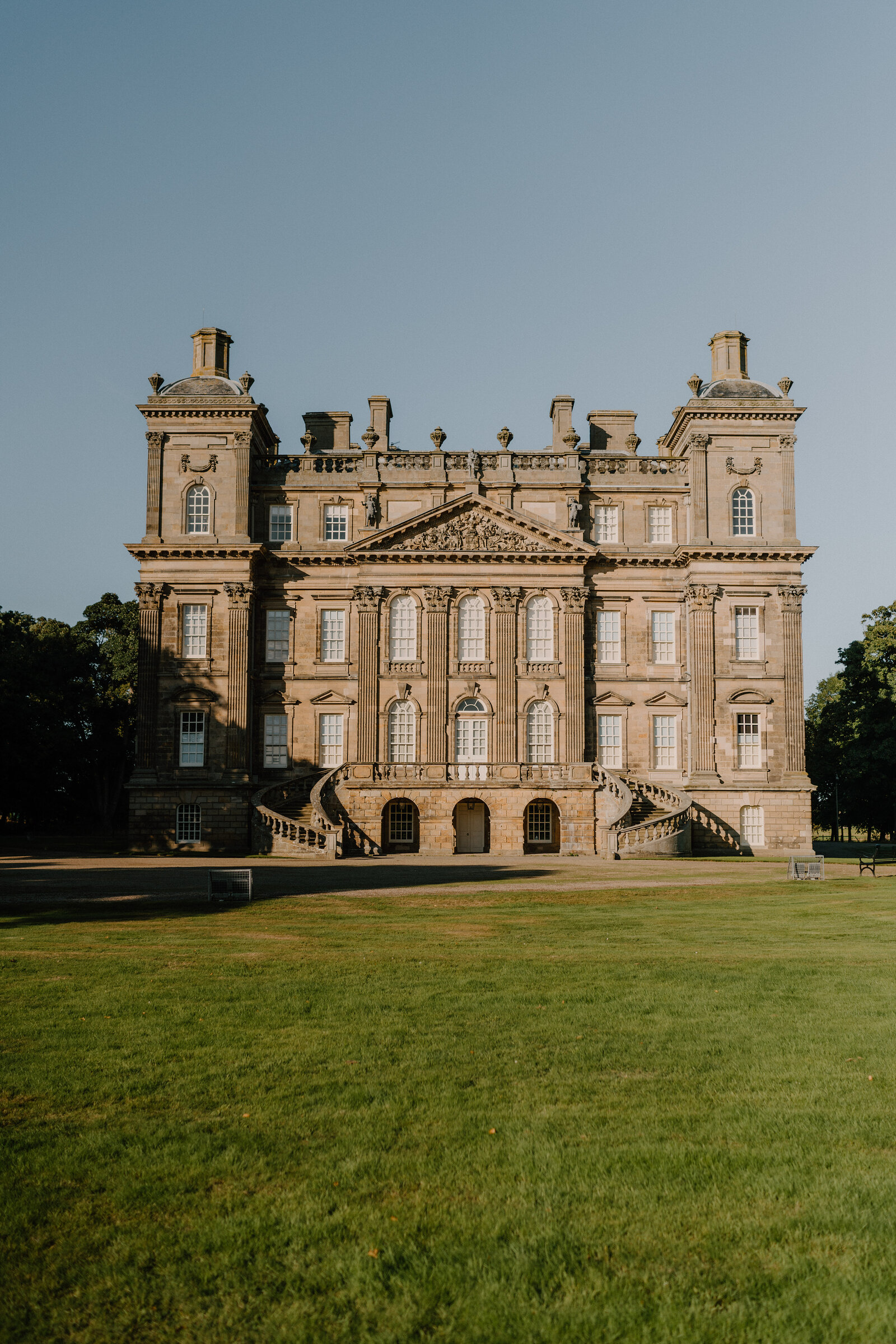 A grand stone mansion with turreted corners and a stepped entrance, seen across an open lawn