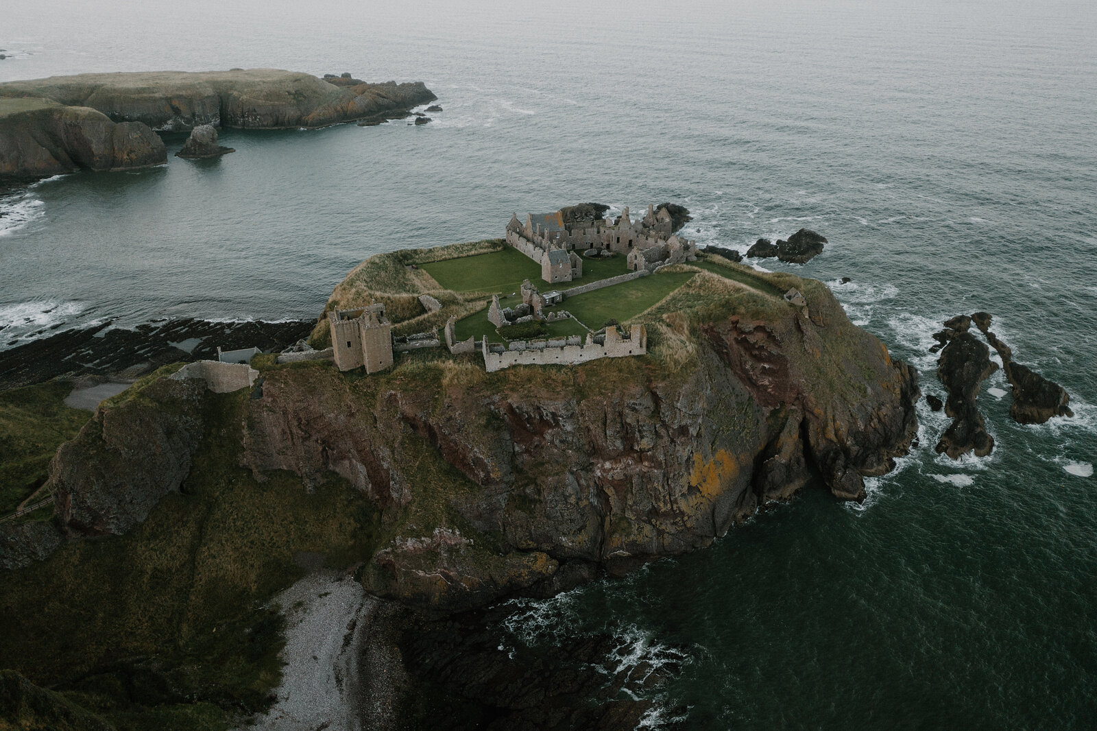 An aerial view of a ruined castle on a rocky headland surrounded by the sea