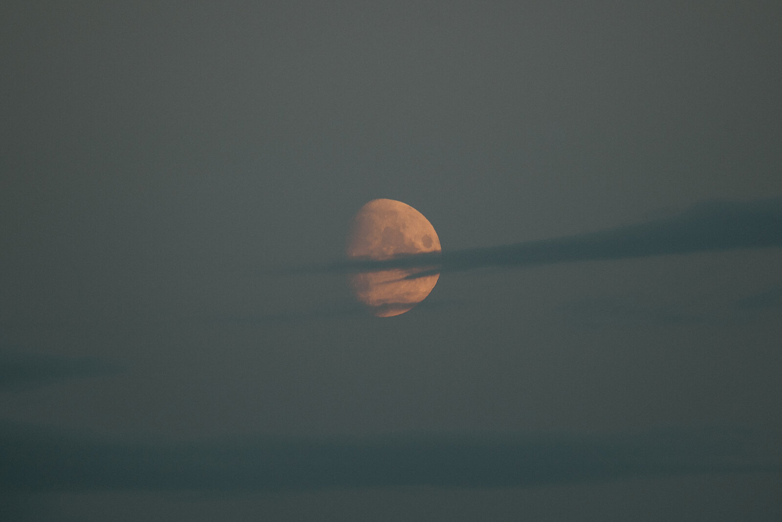 A hazy moon rising above layered clouds at dusk