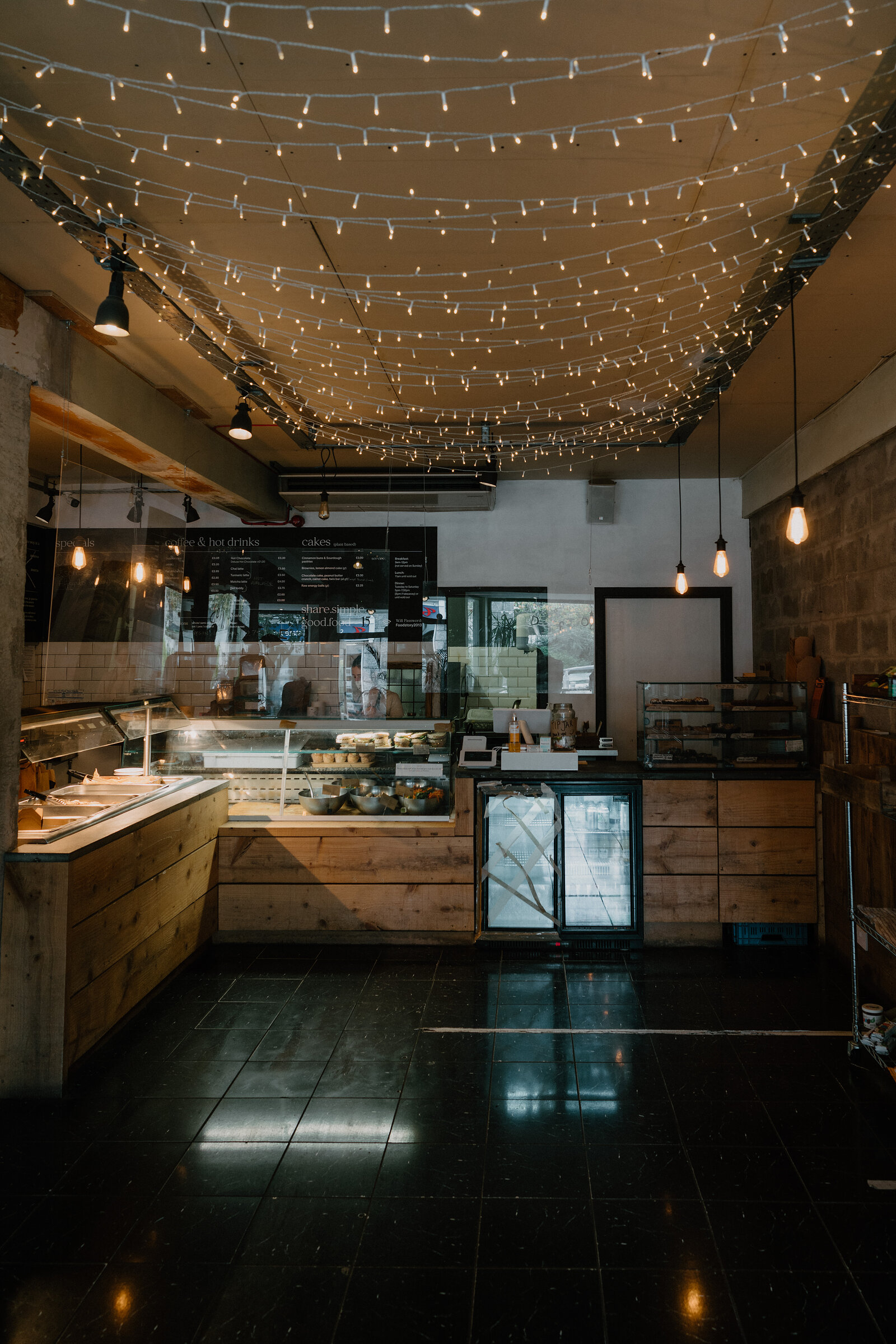 String lights criss-cross the ceiling of a bakery counter lined with pastries and cakes.