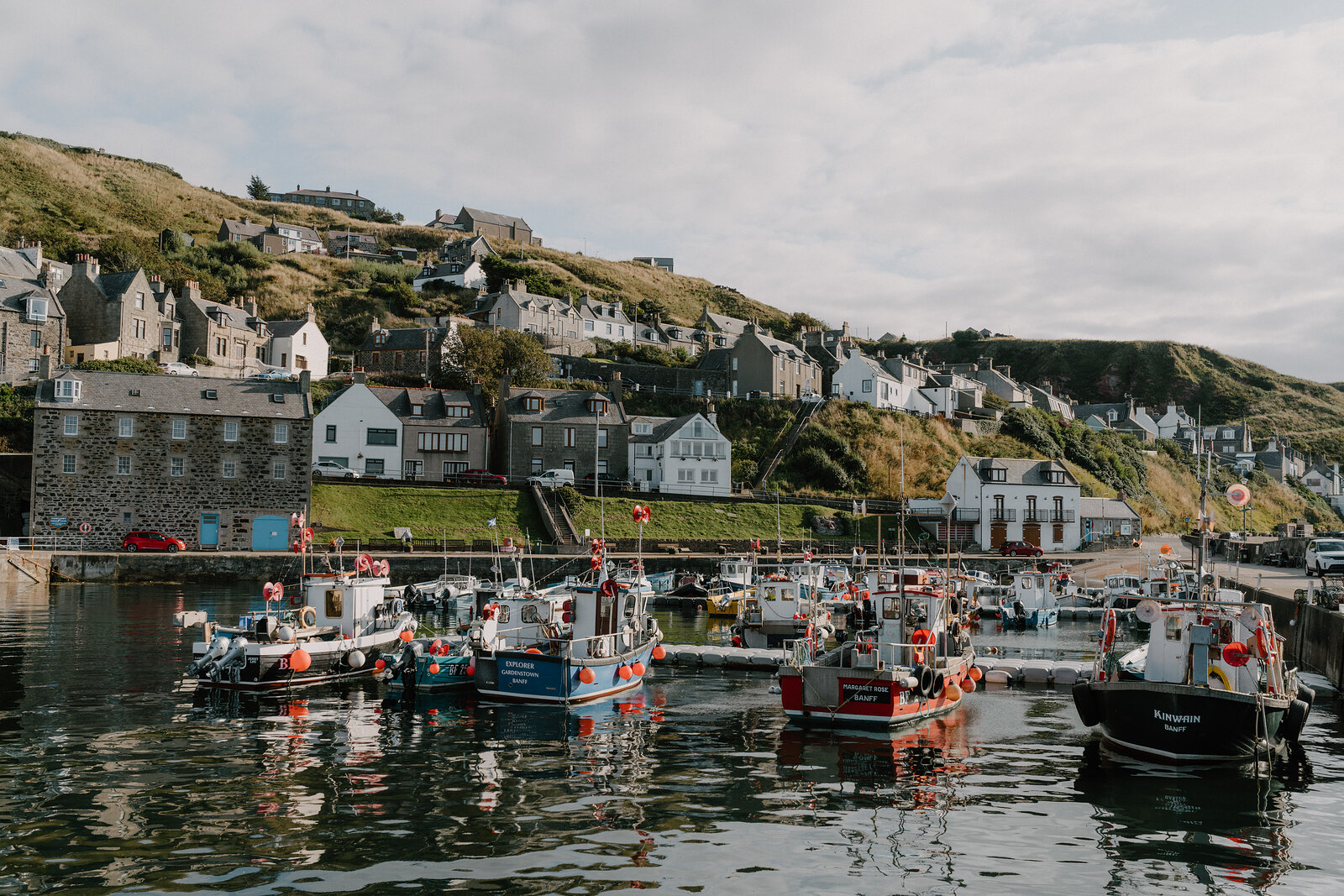 Fishing boats crowd a harbour beneath a fishing village's cottages on the hillside.