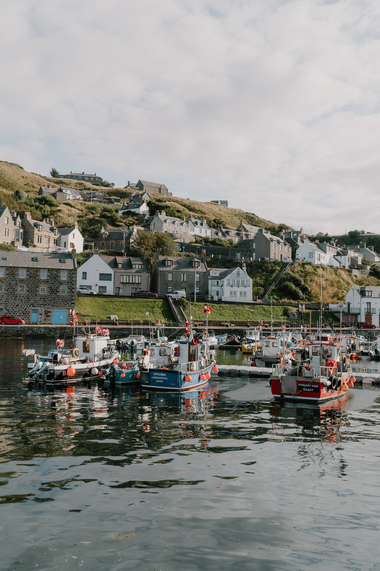 Fishing boats fill a harbour beneath a hillside village of stone cottages.