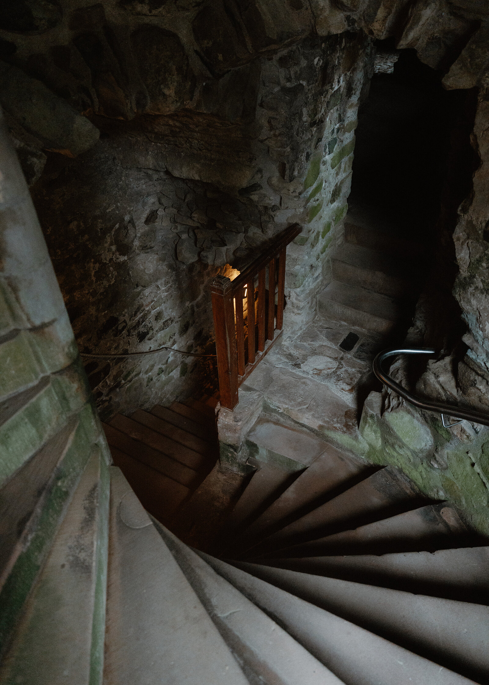 A worn stone spiral staircase inside Huntly Castle, lit by a small window and a wooden handrail