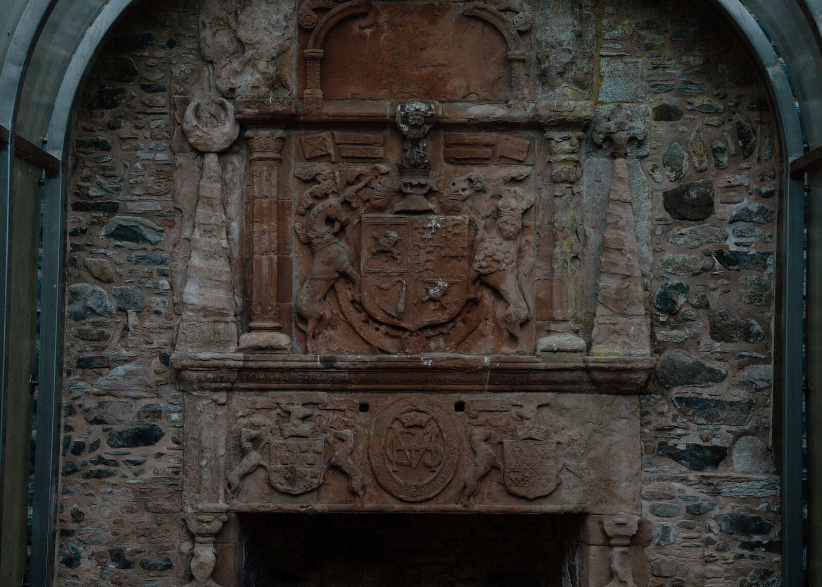 A close view of the carved heraldic panel above Huntly Castle's fireplace, flanked by stone figures