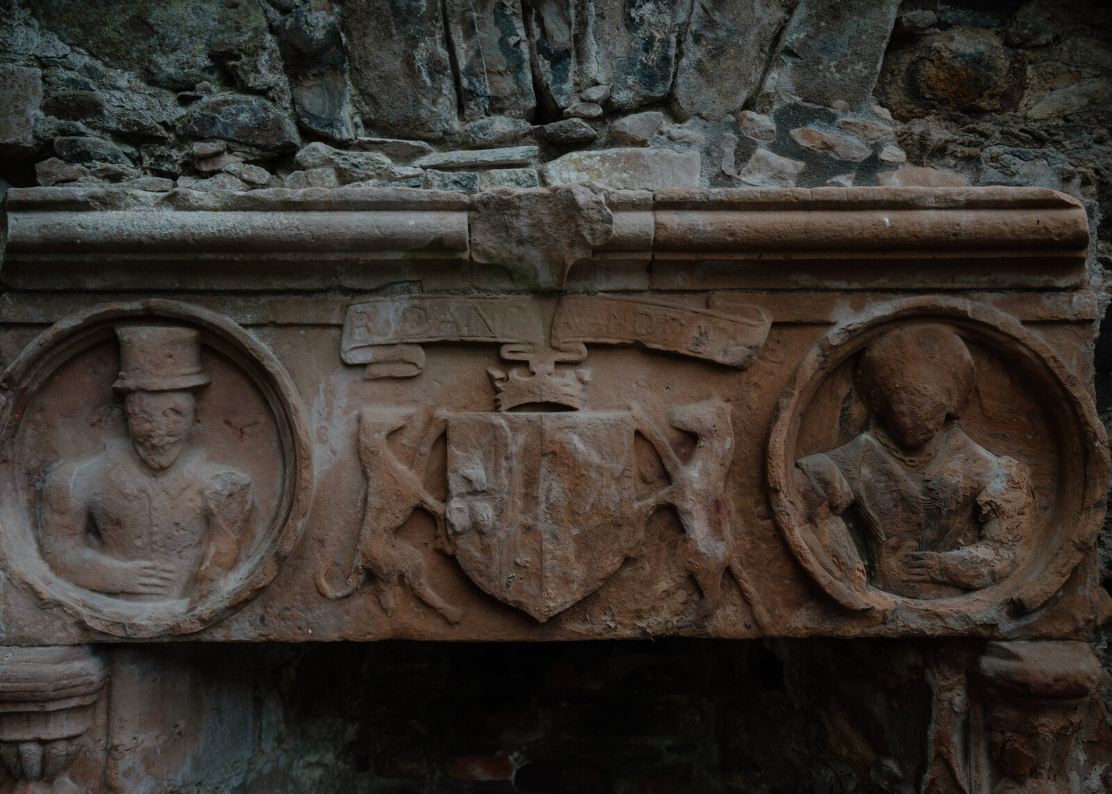A carved stone panel at Huntly Castle with two roundel figures flanking a central coat of arms