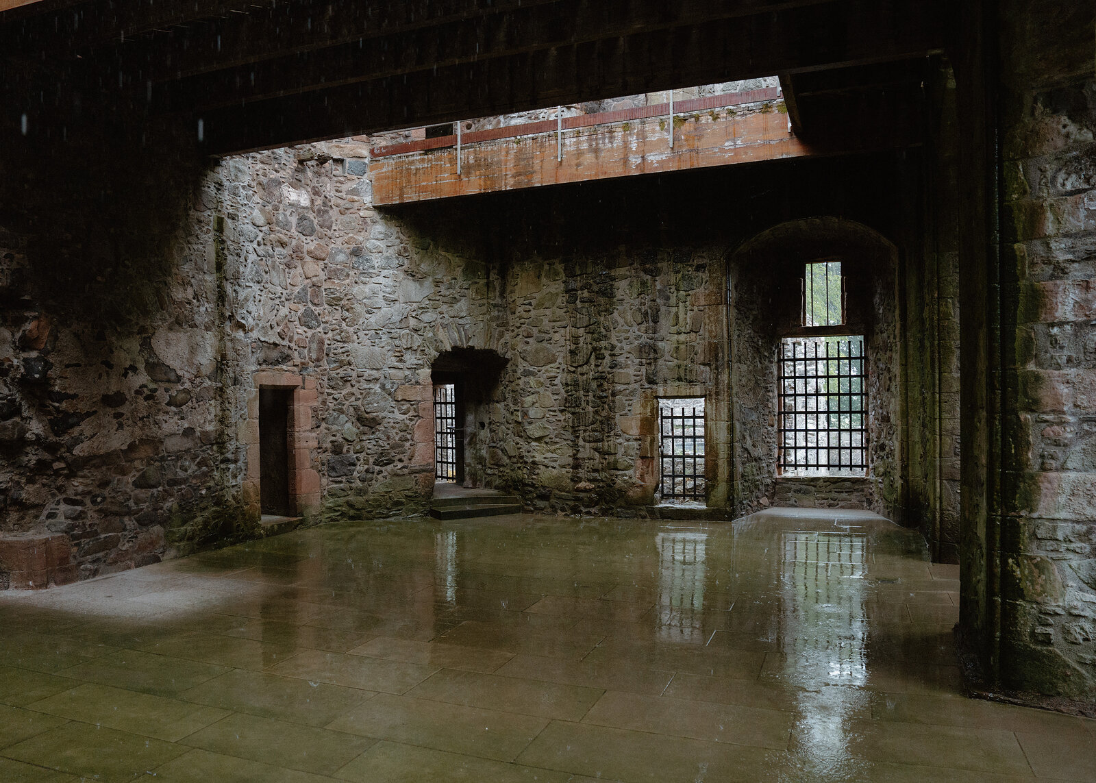 A rain-soaked courtyard inside Huntly Castle, barred windows reflected in the wet flagstones