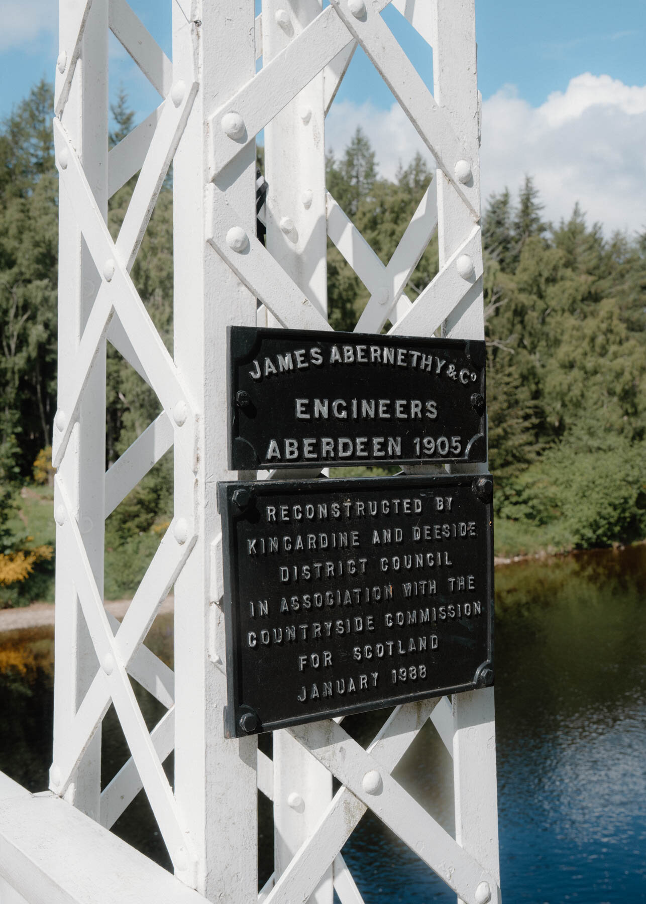 A plaque reading James Abernethy and Co Engineers Aberdeen 1905 mounted on a white suspension bridge tower
