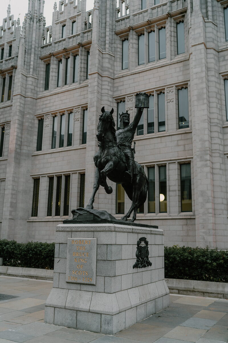 A bronze equestrian statue of Robert the Bruce rises before a Gothic granite tower.