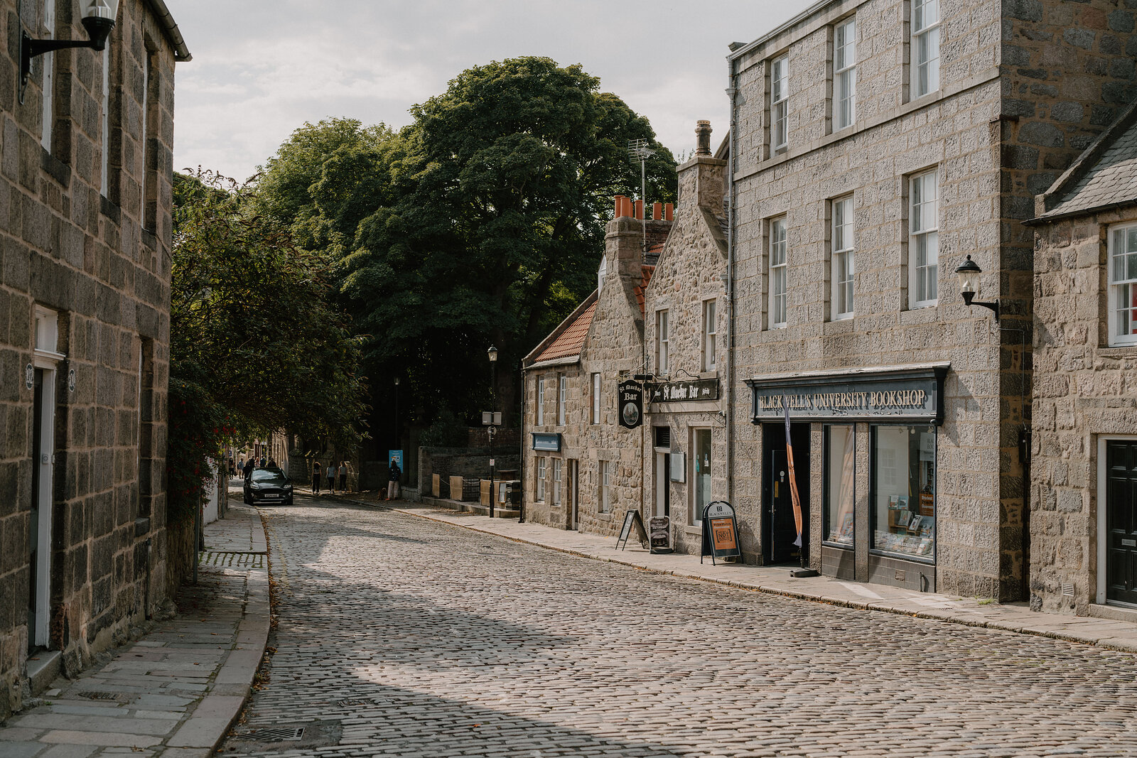 A cobbled Aberdeenshire street lined with granite buildings and a corner shop.