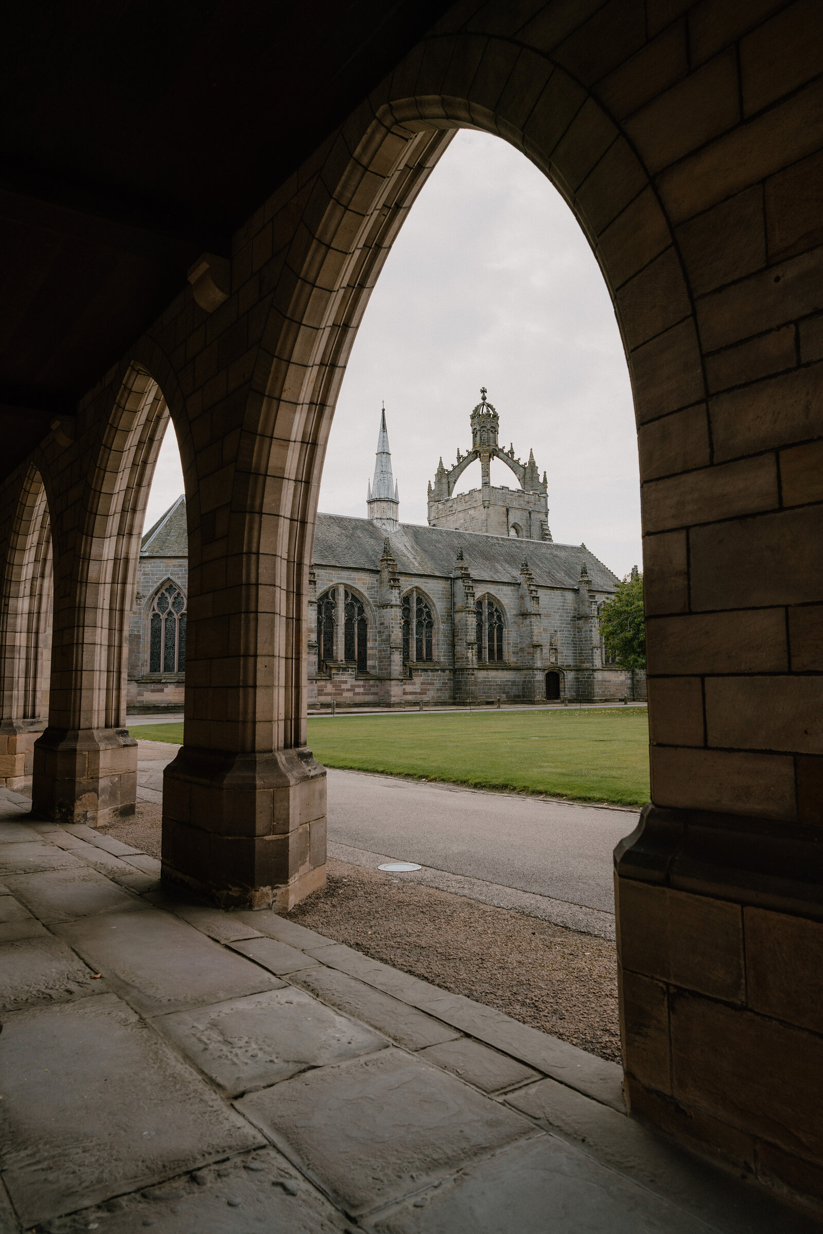 The crown-towered chapel in Aberdeenshire framed through a stone cloister arcade.