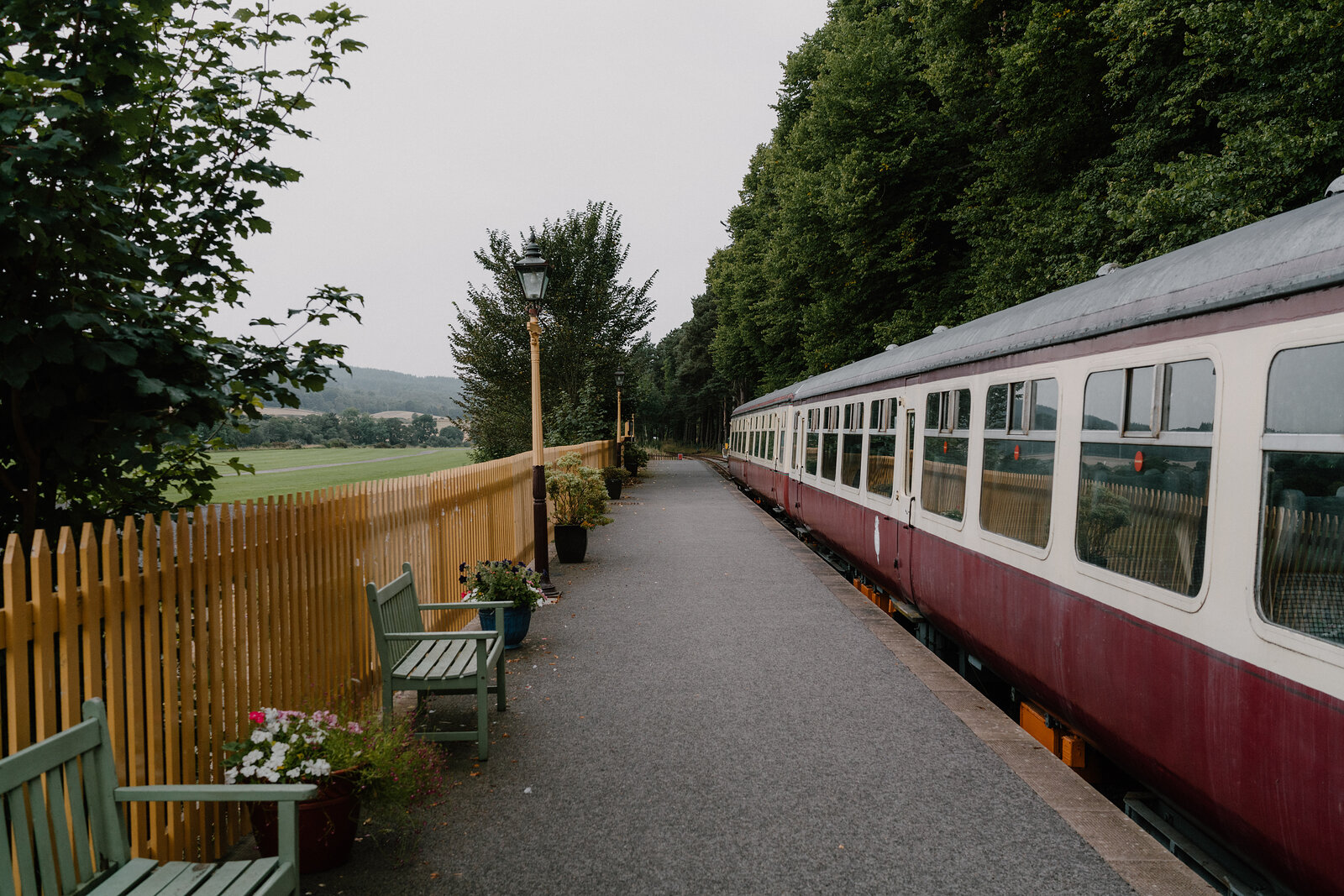 A heritage railway platform in Aberdeenshire, benches and flower baskets beside a maroon and cream carriage.