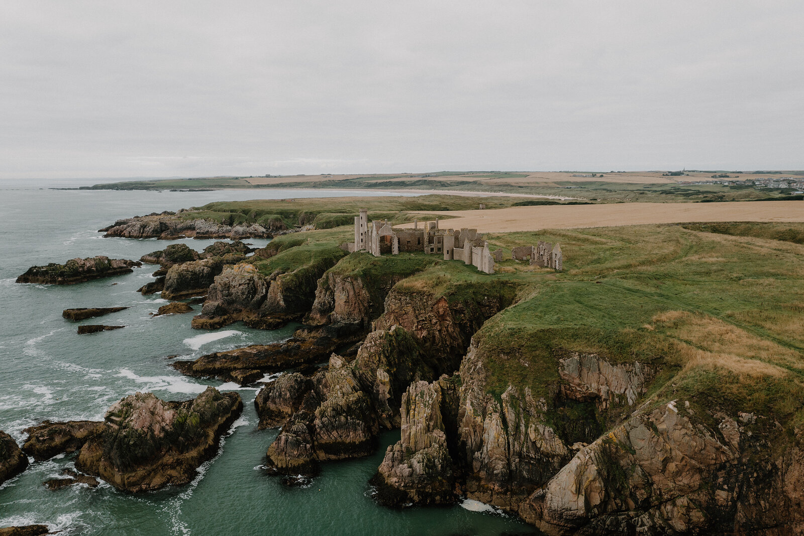 A ruined castle on rugged sea cliffs in Aberdeenshire, farmland stretching inland.