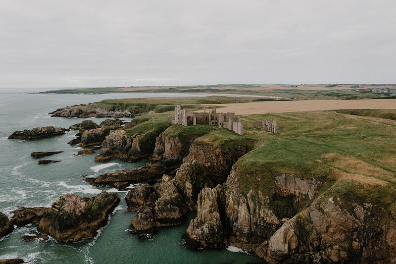 A ruined castle on rugged sea cliffs in Aberdeenshire, farmland stretching inland.