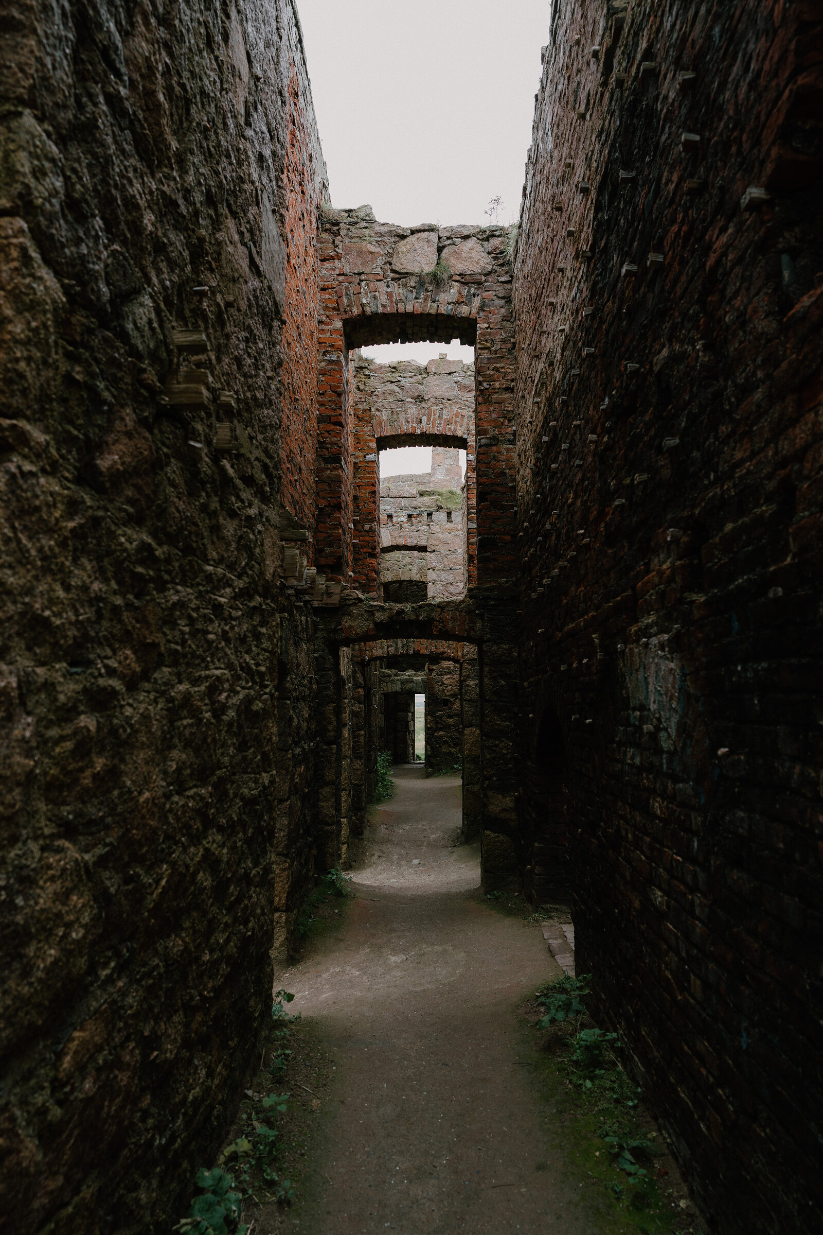 A roofless brick corridor inside a ruined Aberdeenshire castle, arched doorways receding into the distance.