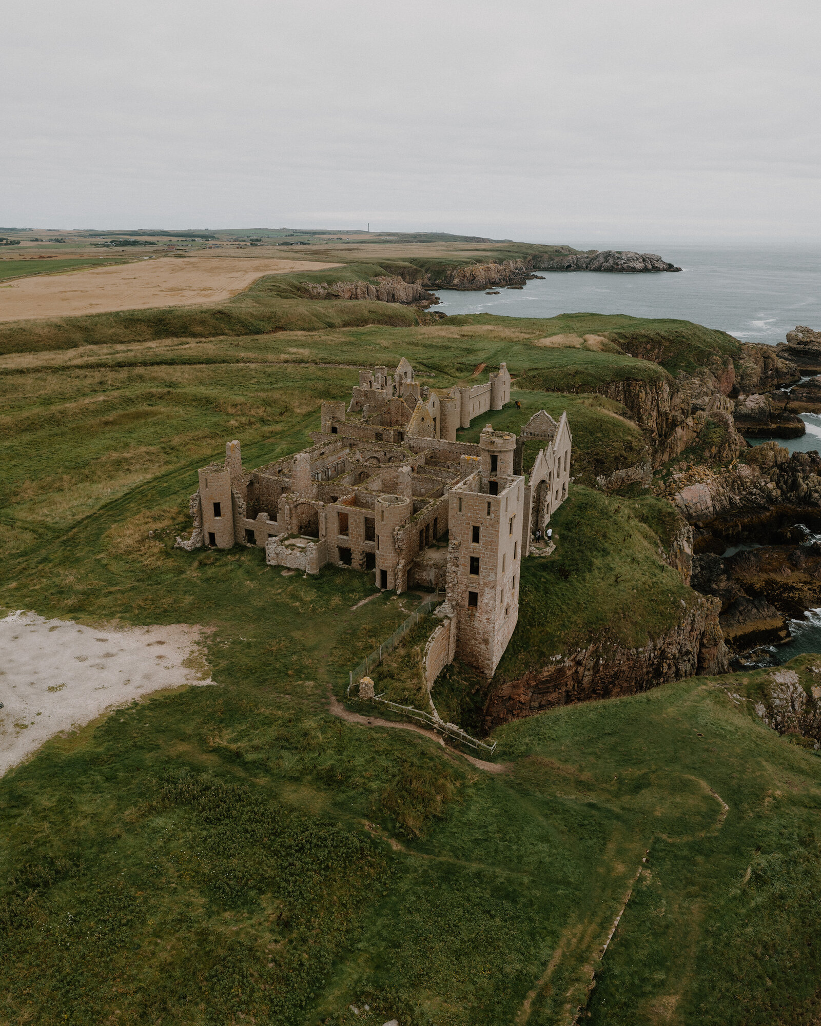 A ruined castle standing on a clifftop above the sea in Aberdeenshire, fields stretching inland.