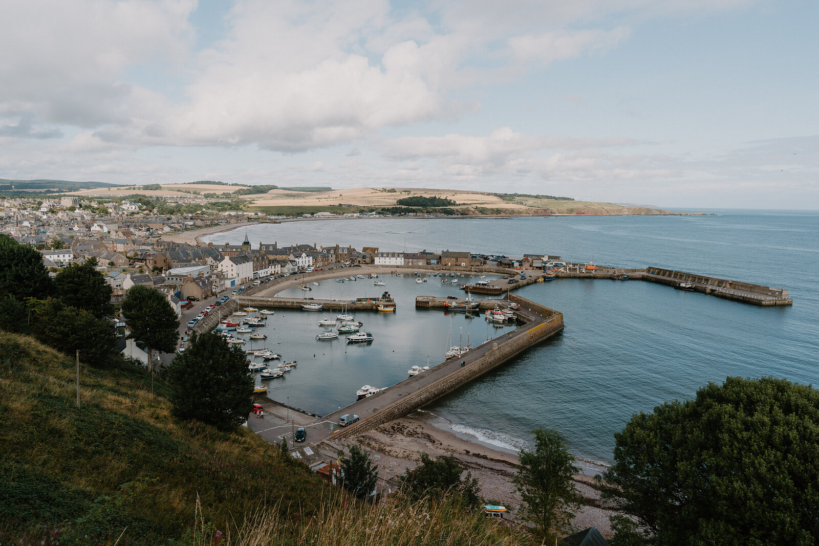 An aerial view of a harbour town in Aberdeenshire, boats moored inside its stone breakwater.