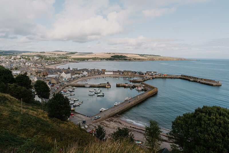 An aerial view of a harbour town in Aberdeenshire, boats moored inside its stone breakwater.