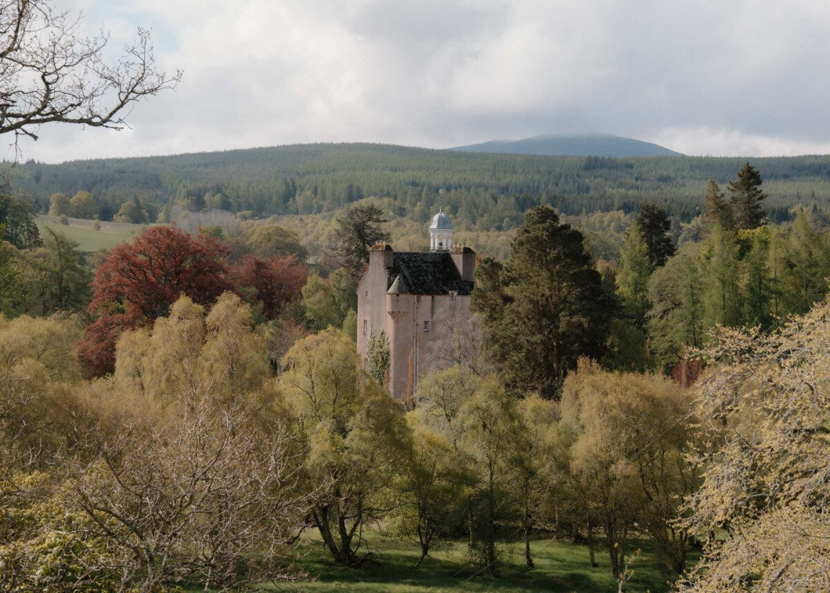 A turreted tower with a small cupola is glimpsed through autumn-coloured trees, hills in the distance