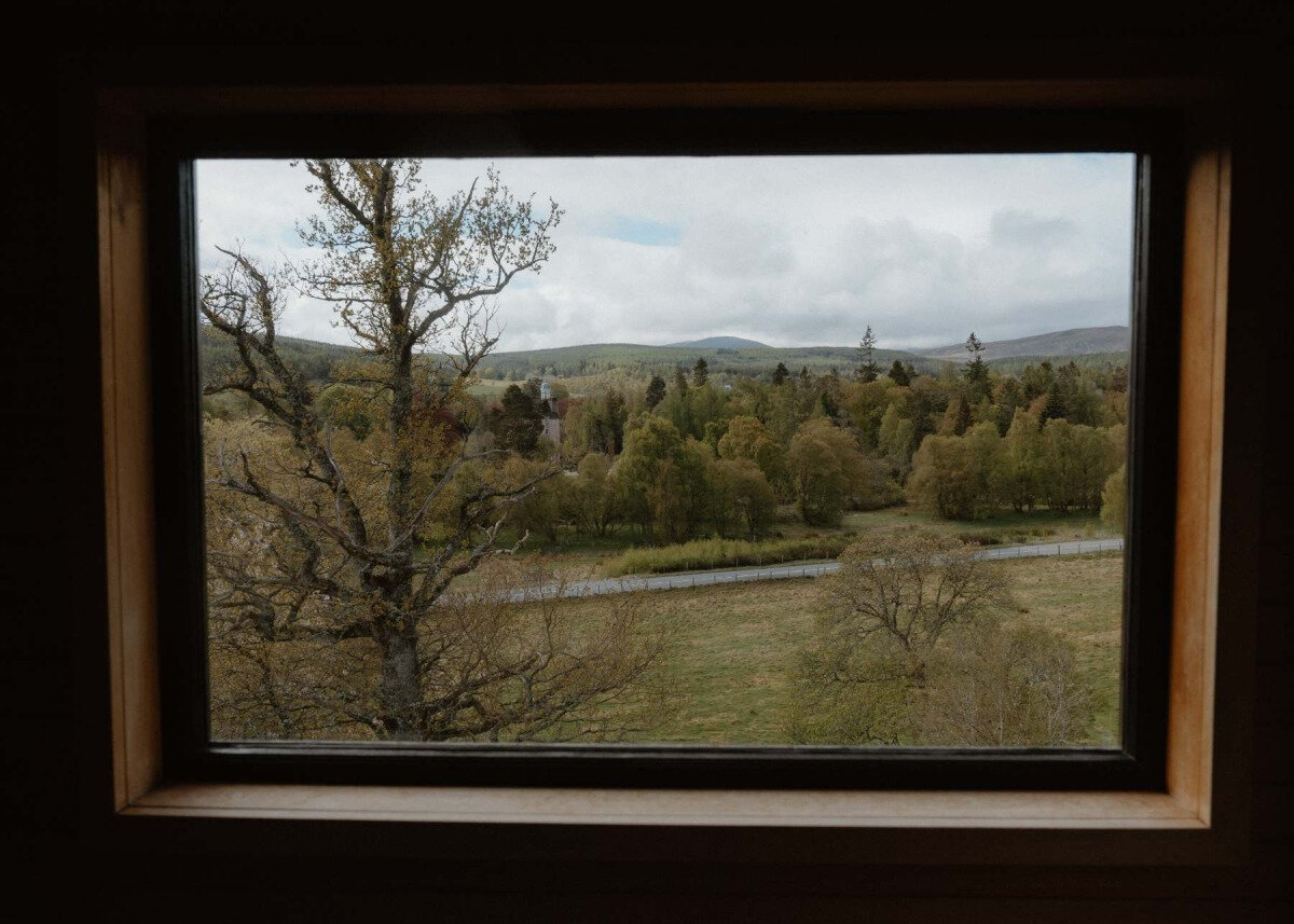 A timber-framed window looks out over a river valley towards a distant church spire, at Stravaig Saunas