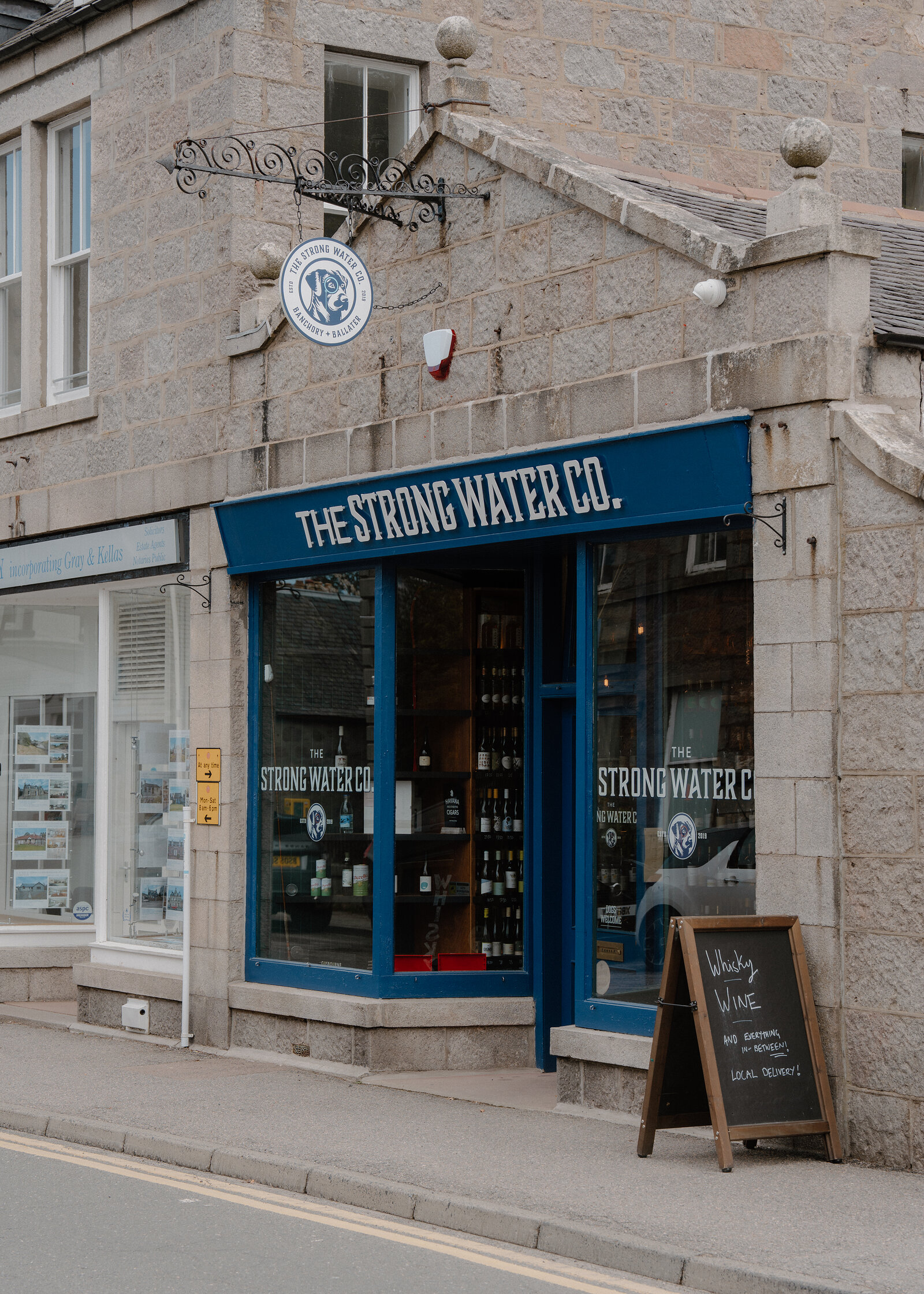 The Strong Water Co shopfront with blue-framed windows and a sandwich board advertising whisky and wine