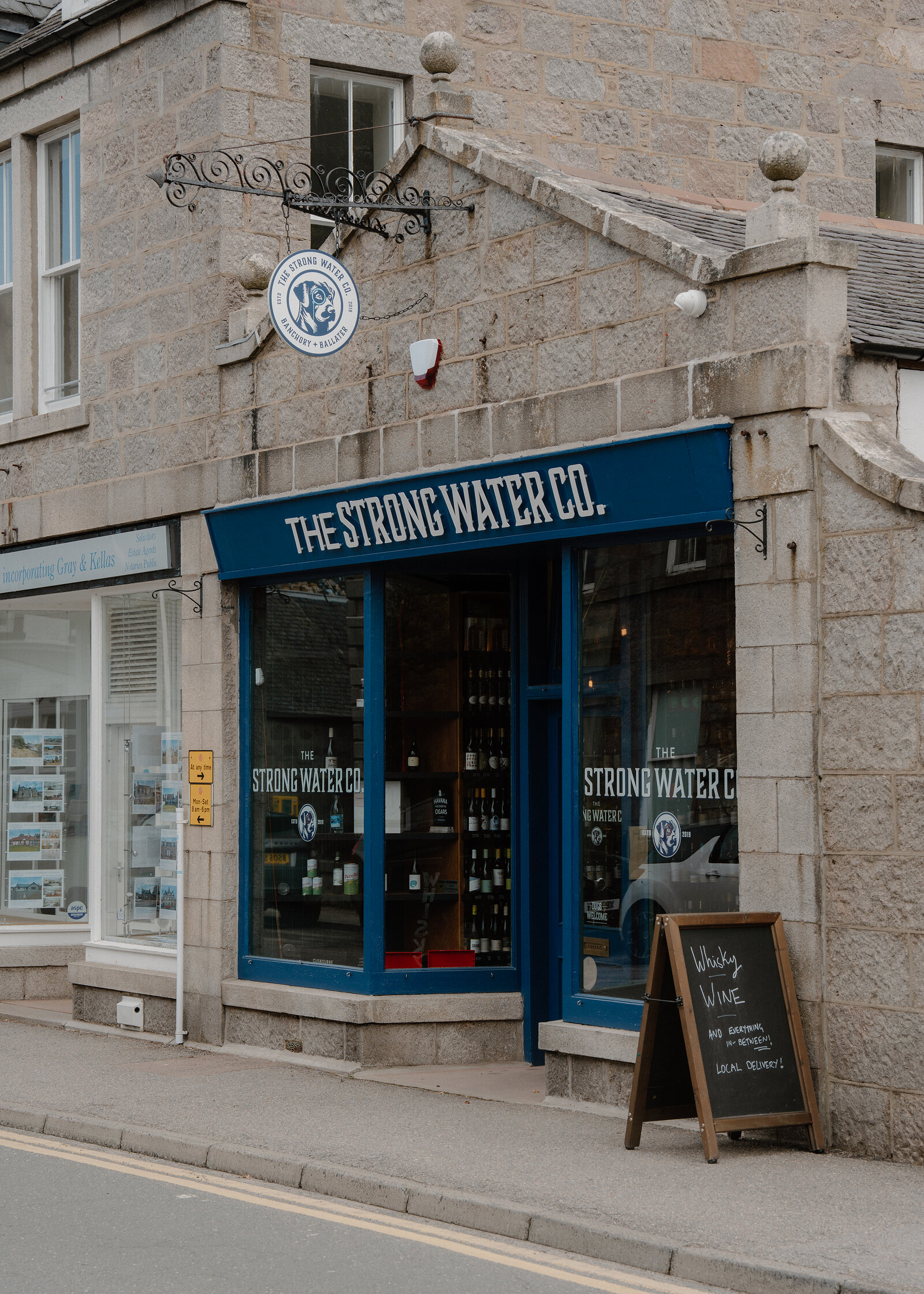 The Strong Water Co shopfront with blue-framed windows and a sandwich board advertising whisky and wine