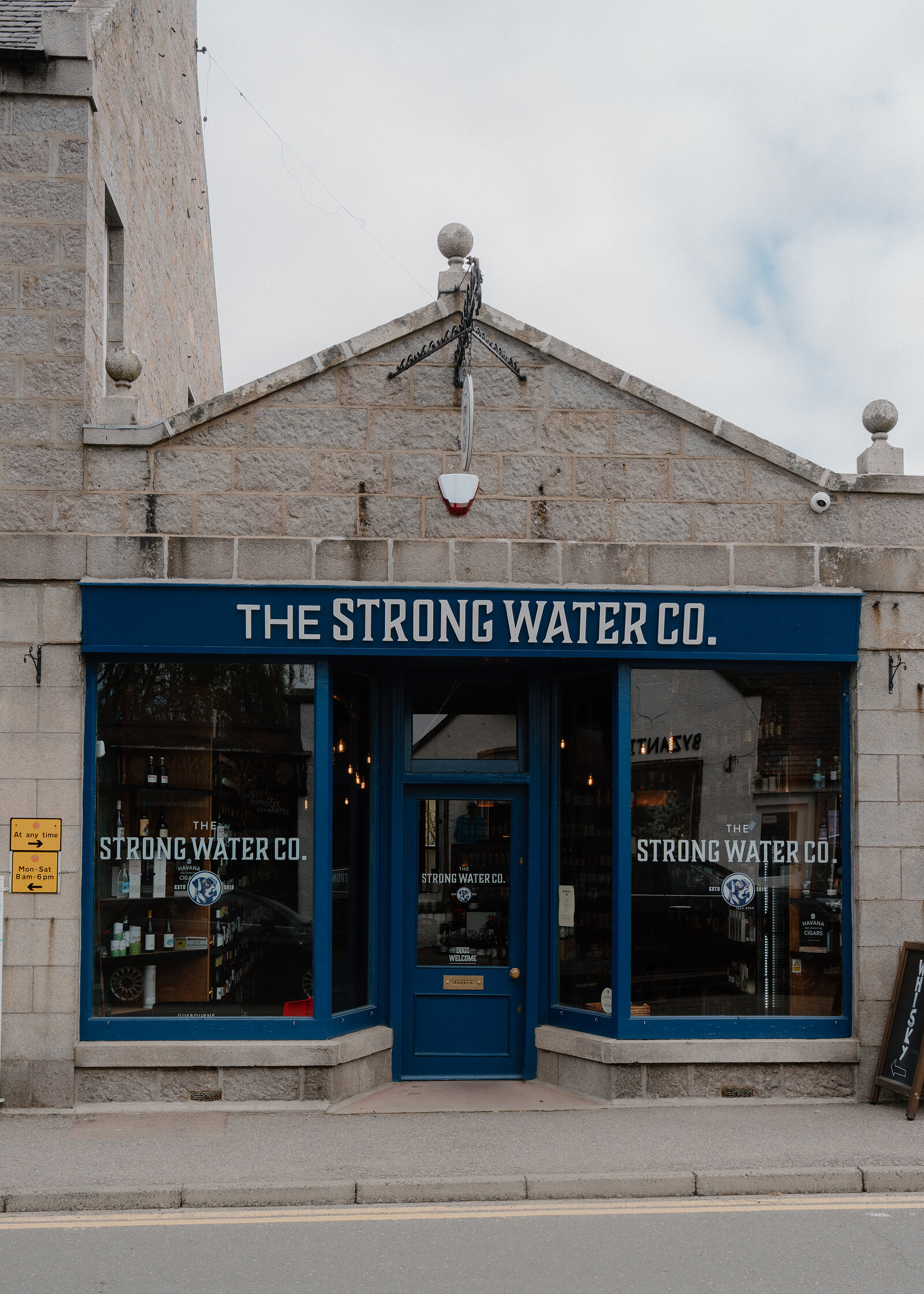 The Strong Water Co shopfront with blue-framed windows beneath a stone gable and hanging lantern