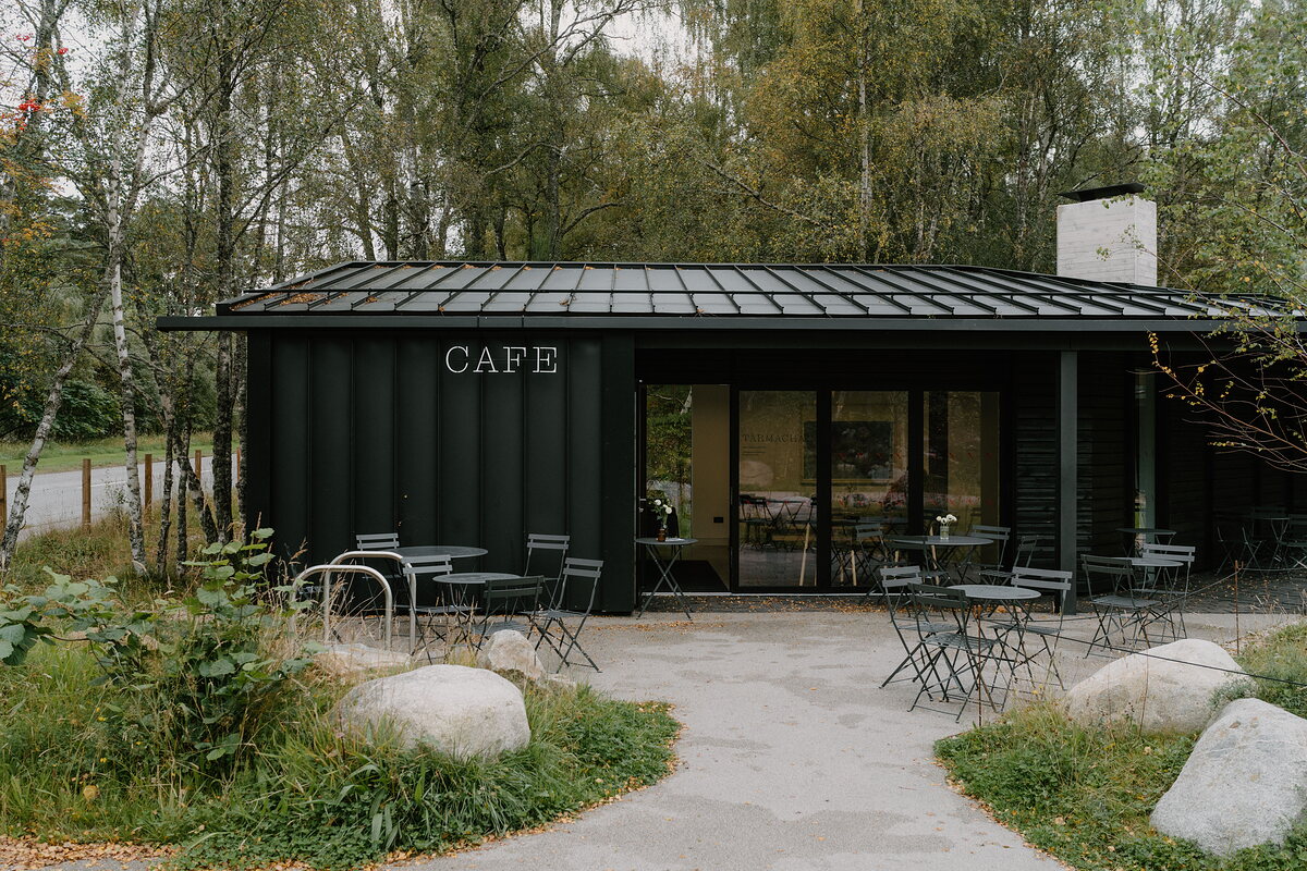 A black shipping-container building with a plain sign reading Cafe stands by the shore.