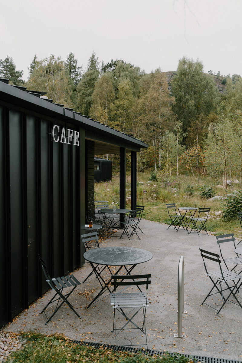 A black container-style café stands among trees, bistro tables set outside.