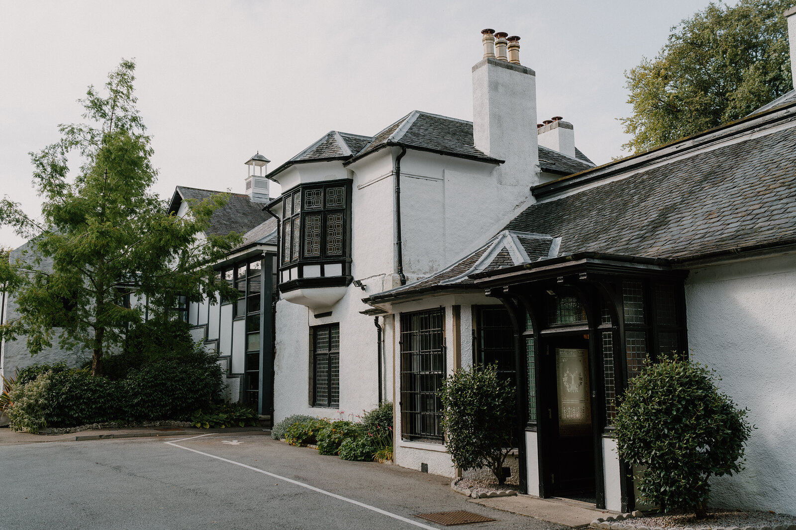 A white Victorian building's bay windows and chimneys rise above a gravel courtyard.