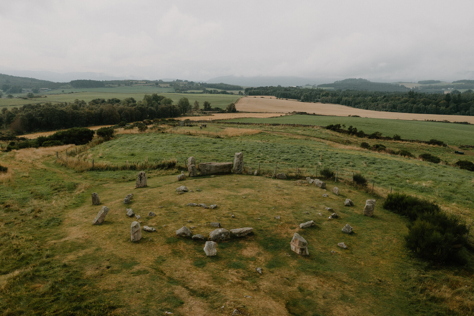 A ring of standing stones sits in a field, seen from above.
