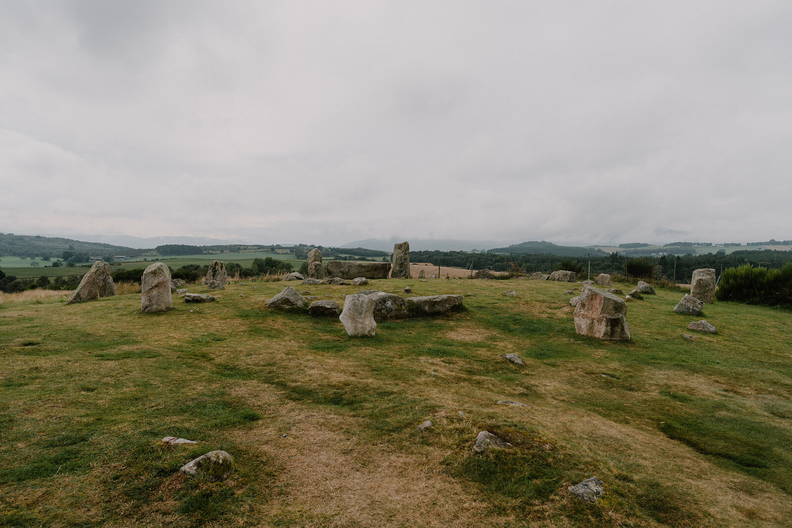 A ring of standing stones sits in a grassy field.