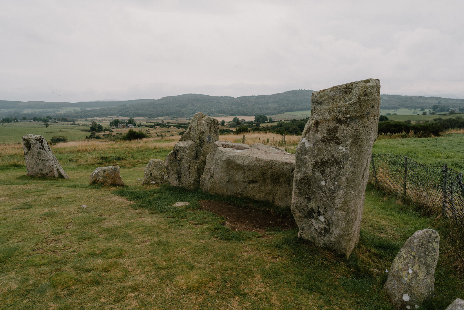 A large capstone rests on upright stones, forming an ancient chambered cairn in a field.