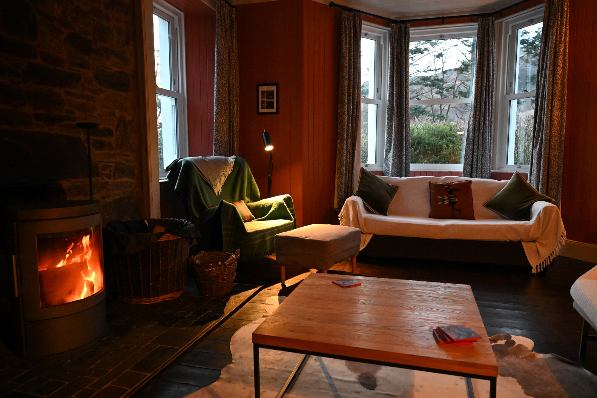 A bay window, a sofa and an armchair, and the stove alight in the corner of the sitting room.