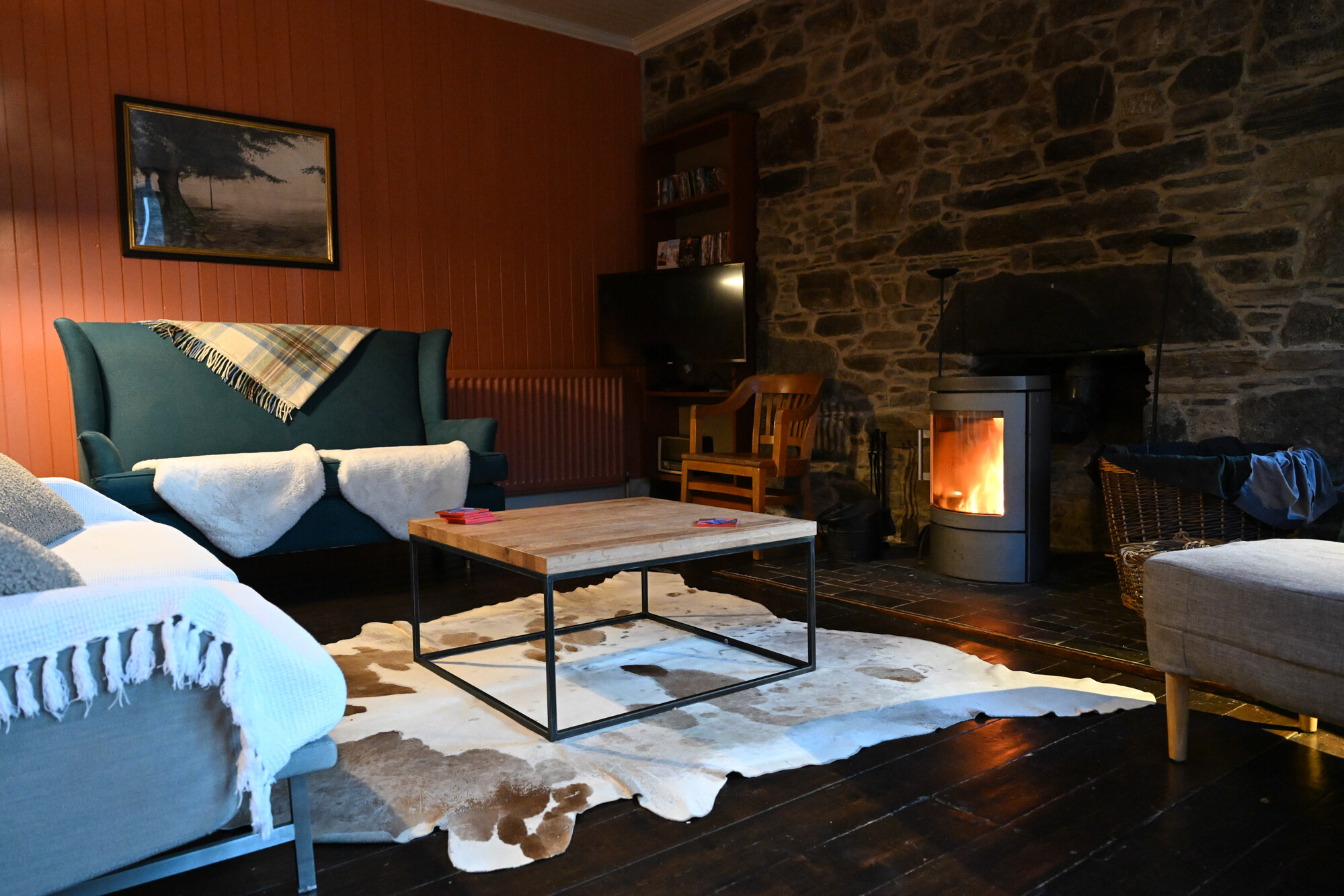 The sitting room: a stone wall with a wood stove burning, sofas with throws, a cowhide rug and a low table.