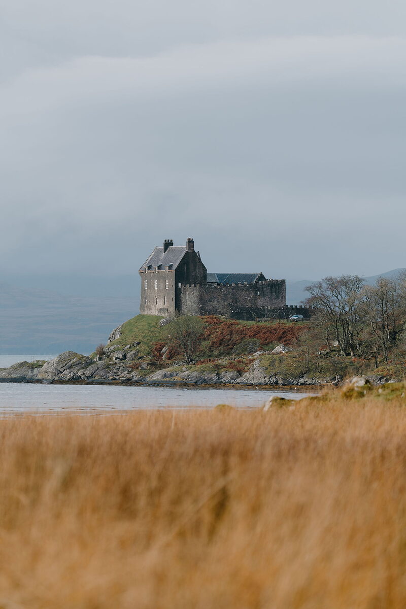 Duntrune Castle stands on a headland above the loch, autumn colour lining the shore beside it.