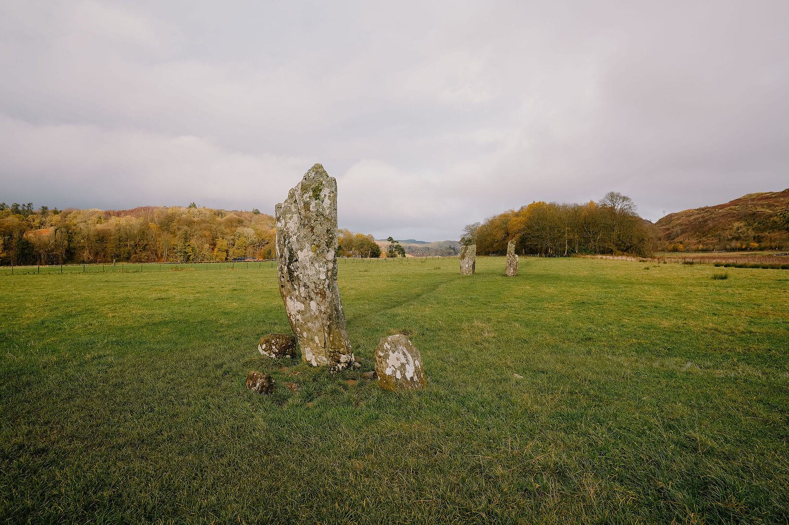 Standing stones set in a grassy field, hills and trees stretching to the horizon