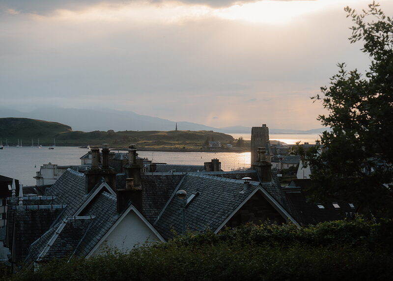 Oban's rooftops and chimney pots silhouetted against a glowing sunset over the bay.