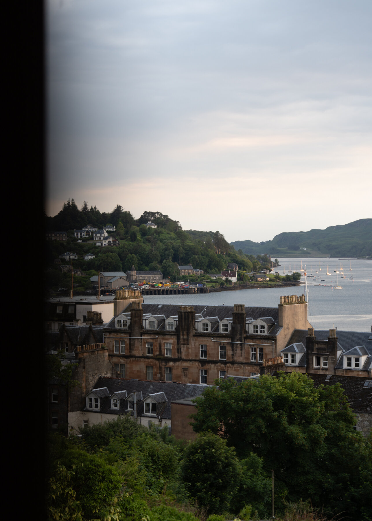 Oban's sandstone tenements and harbourfront seen from a window, boats moored across the bay towards the pier
