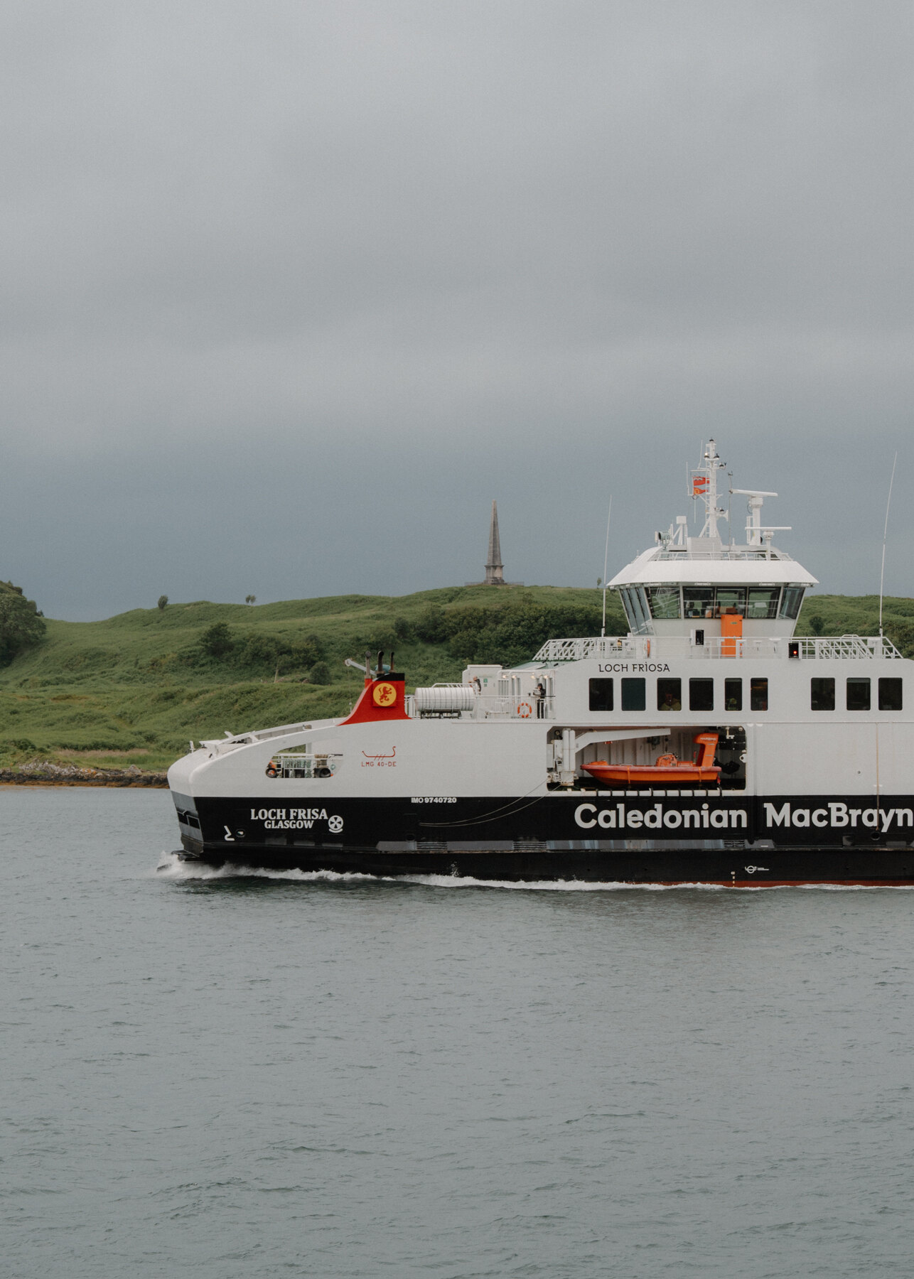 A Caledonian MacBrayne ferry named Loch Frisa crosses Oban's bay, a monument visible on the hillside.