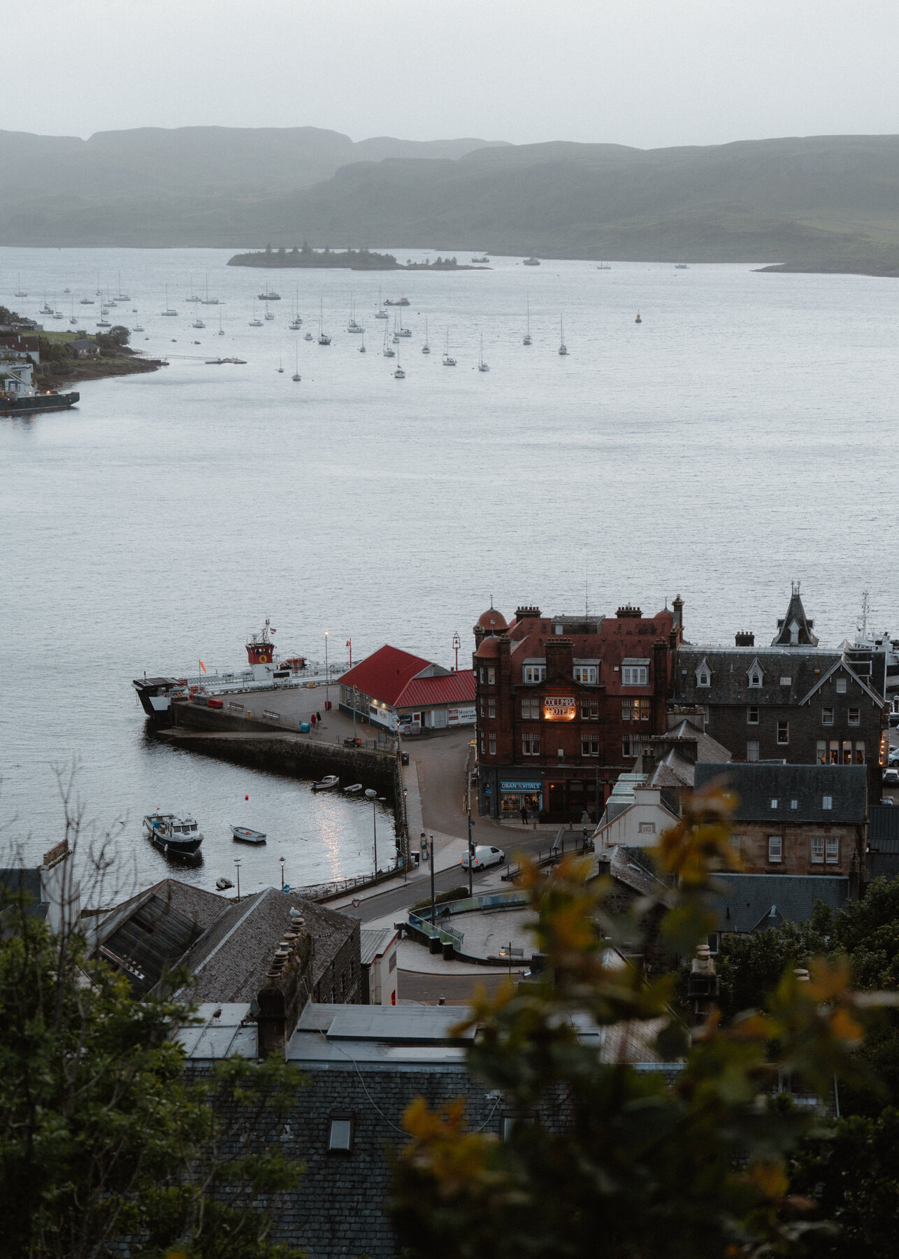 Sailboats scatter across Oban Bay beneath a ferry docked at the harbour.